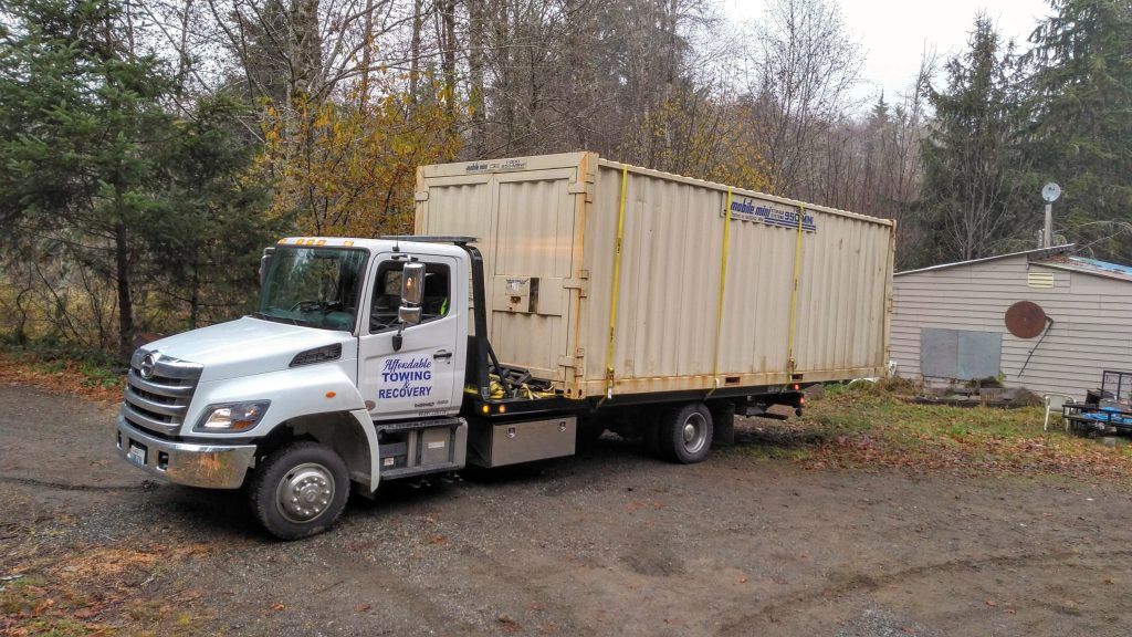 A white tow truck is parked next to a large white container.