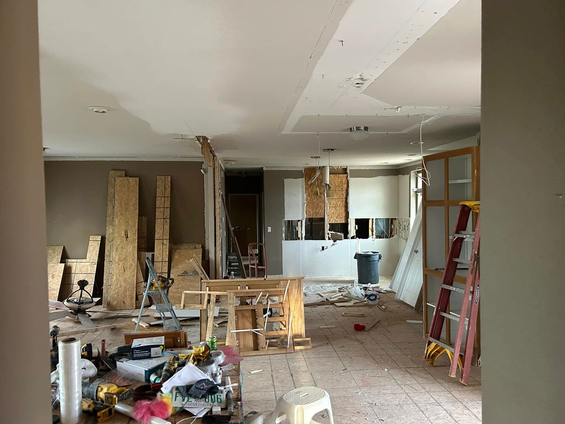 Interior room during renovation, filled with construction materials, exposed walls, and tools; a ladder stands nearby.