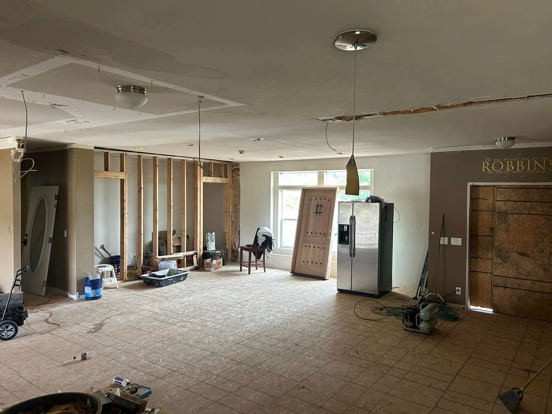 Interior of a house under renovation, with exposed framing, debris, and a refrigerator.