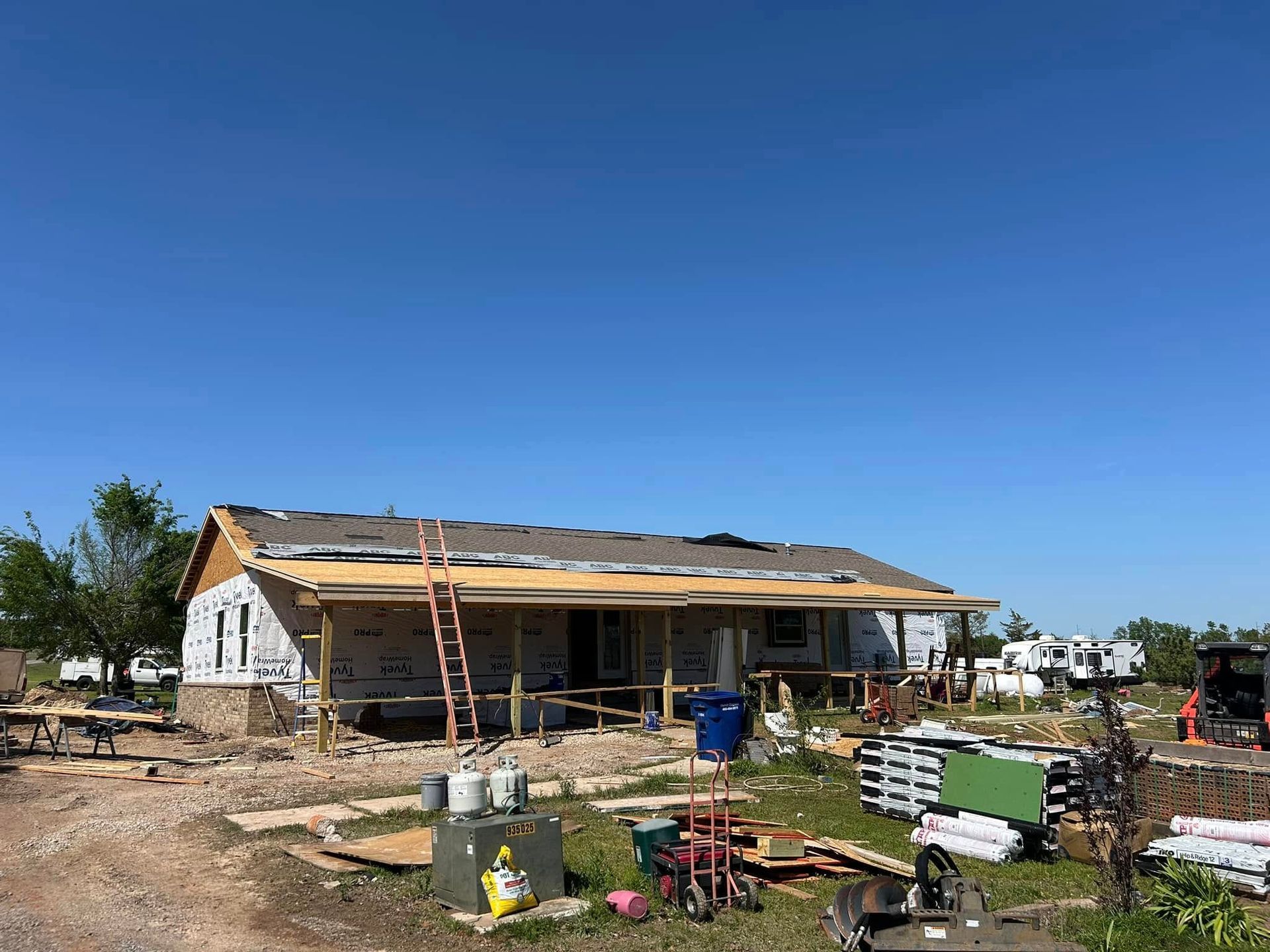 House under construction; wood frame with partial brick facade, roof materials, sunny outdoor setting.