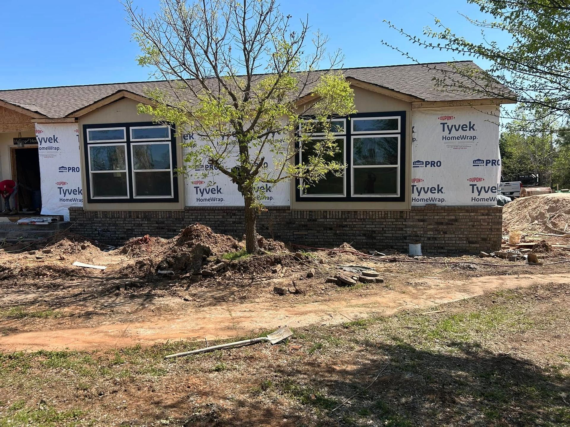House under construction with windows and brickwork, on a dirt lot.