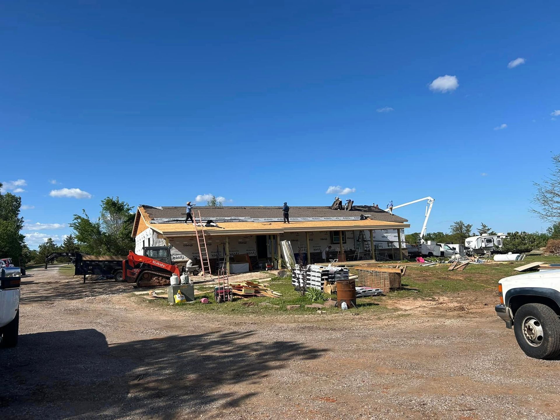 House under construction, workers on roof, clear blue sky, debris on the ground.