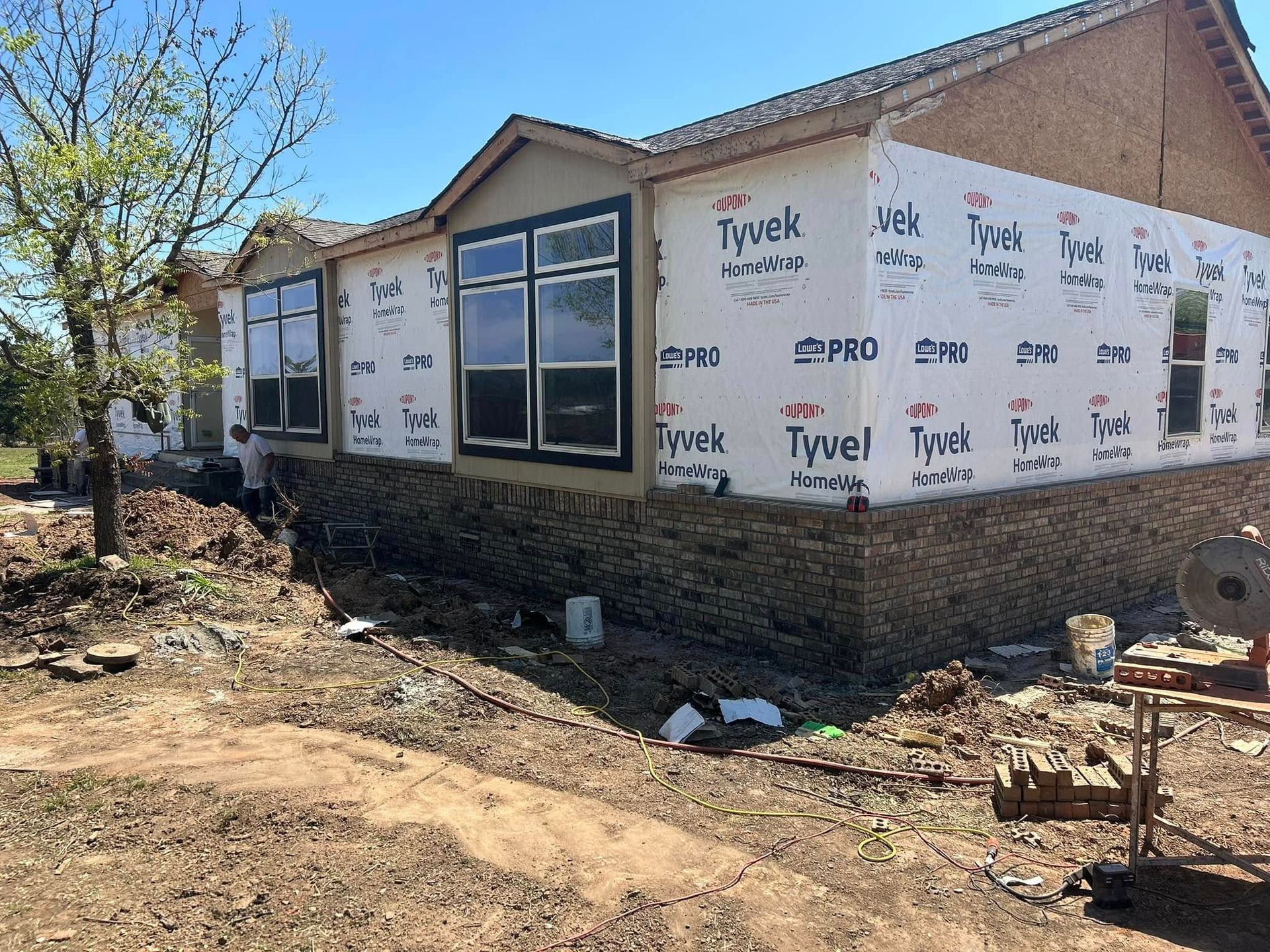 Construction site with house. Exterior walls covered in Tyvek. Brickwork on the lower portion, windows installed.