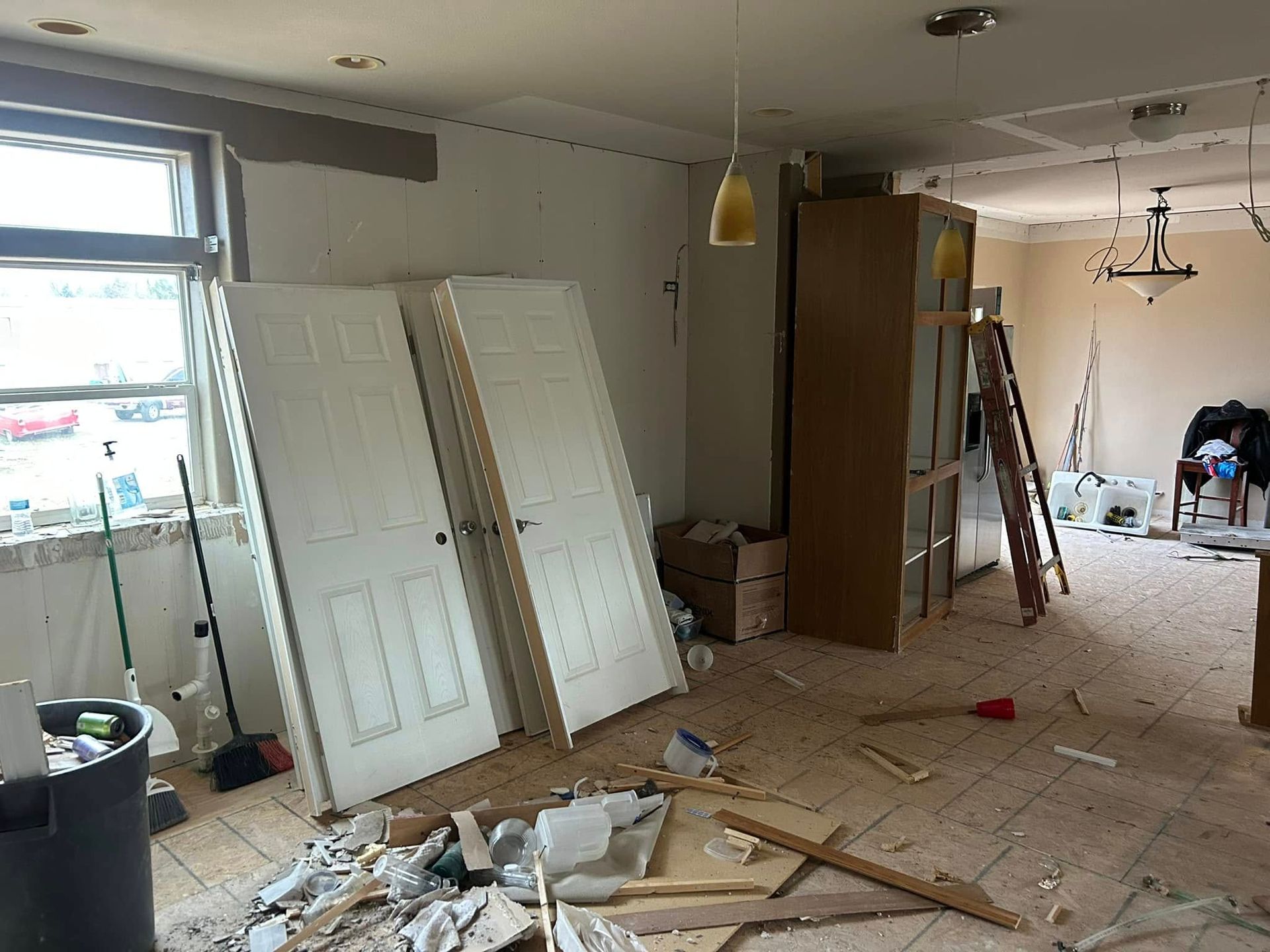 Interior room in disarray during renovation with doors propped against a wall, debris on the floor.