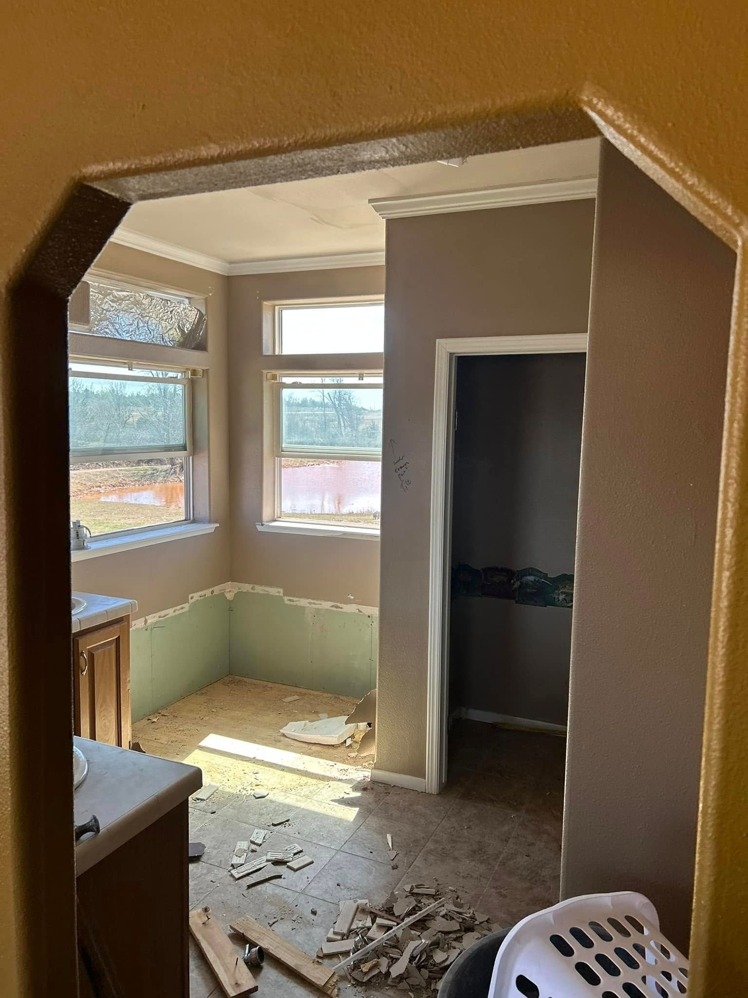 View through an archway into a room with windows and a door; demolition debris on floor.
