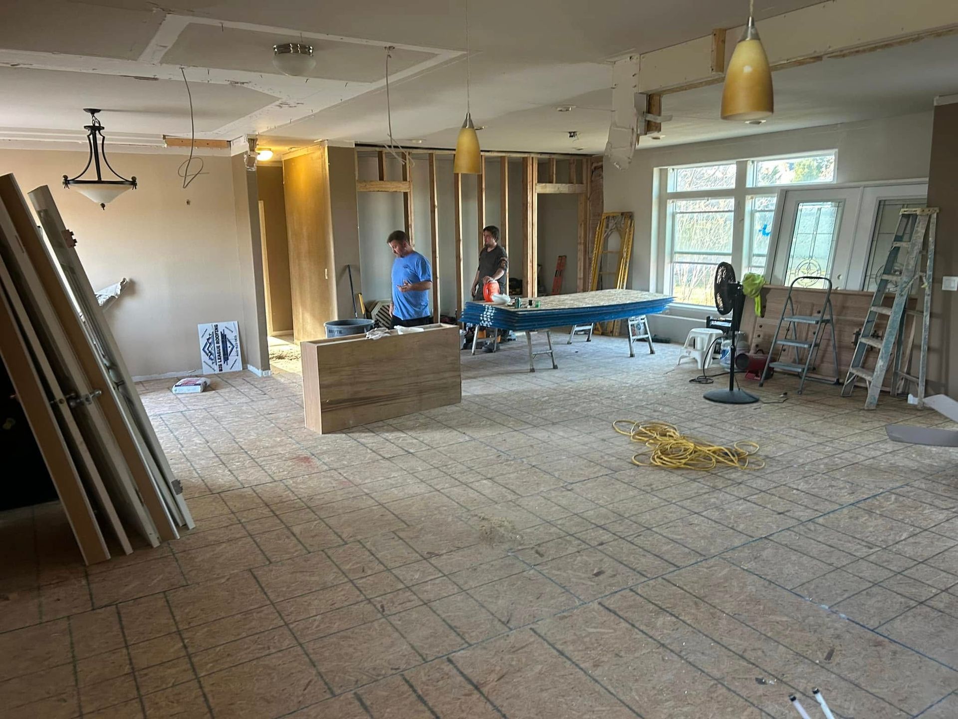 Construction site, interior room with workers, exposed framing, and materials.
