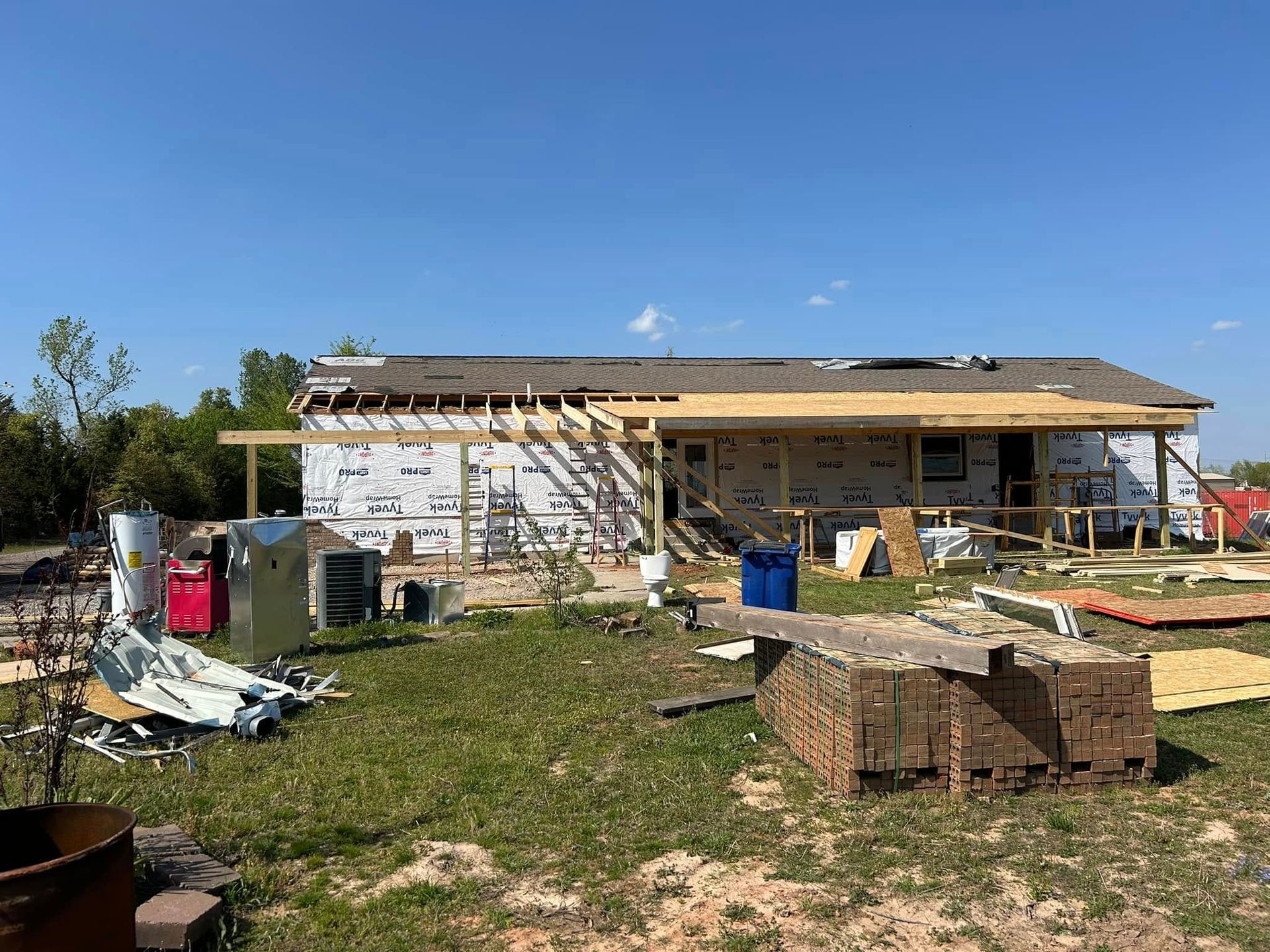 House under construction; wooden framework, siding, and wrap, blue sky.