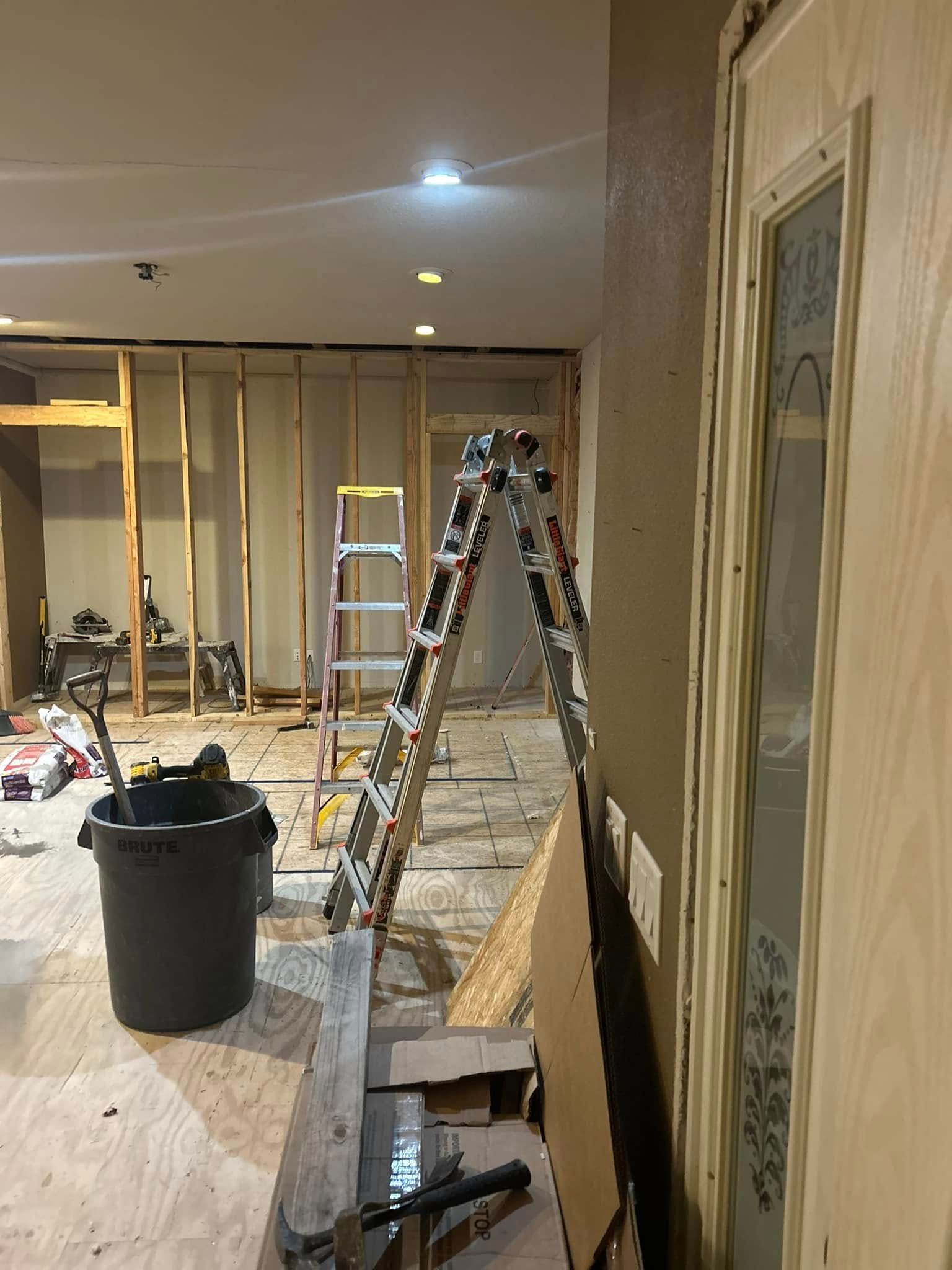 Construction in a room: studs, ladder, bucket, door, debris on the floor.