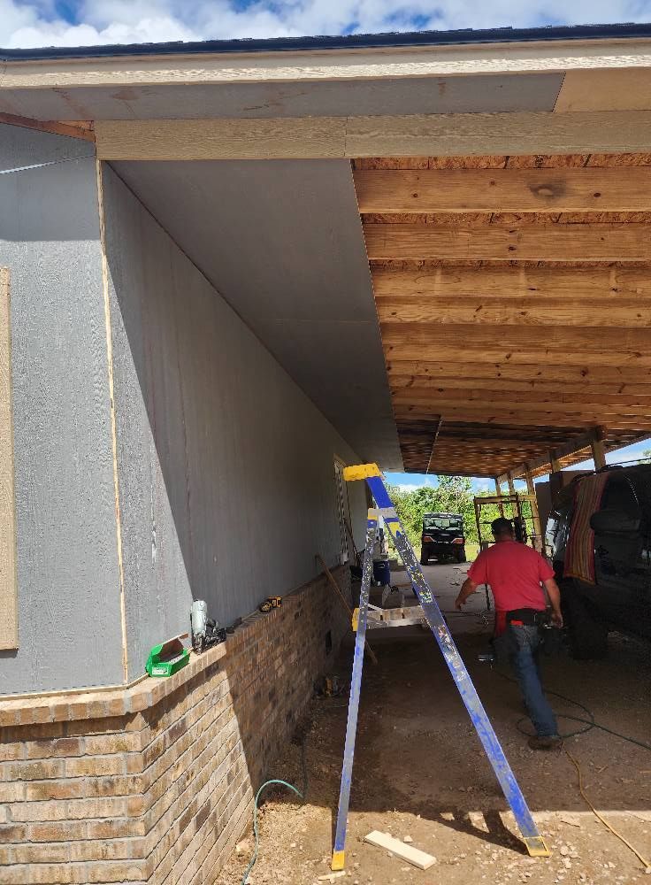 Man working on a building's exterior, using a ladder. The building has gray siding, brick, and exposed wood.