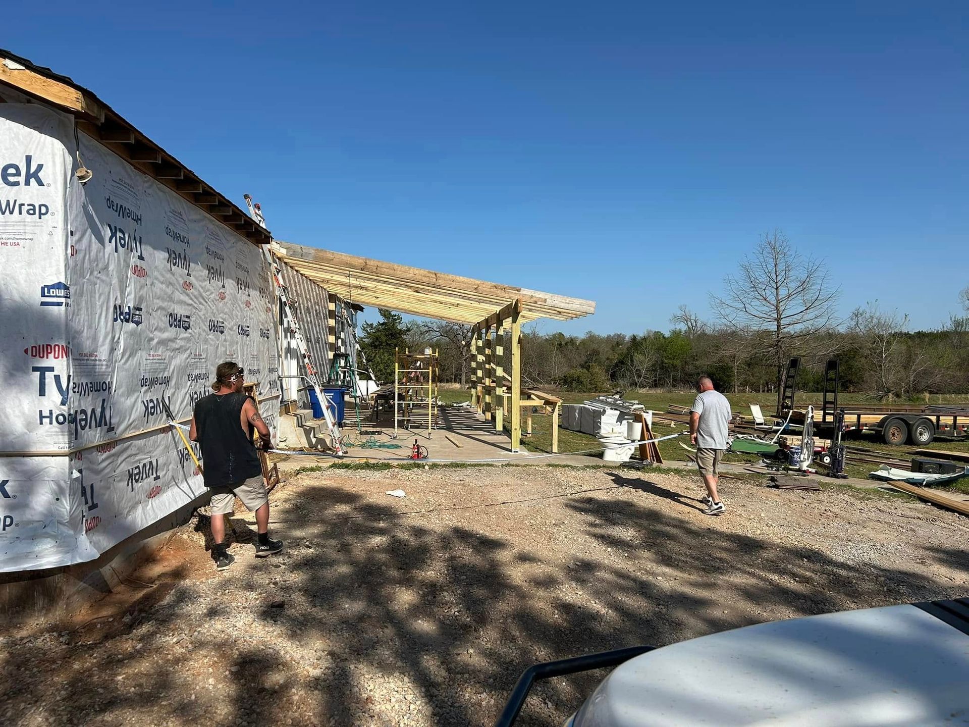 Construction site with workers building a porch. Sunny day. Gravel ground. Blue sky.