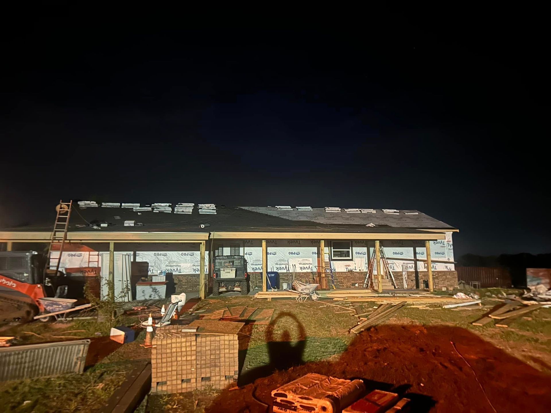 Construction site at night; house with exposed beams, partially completed roof, and building materials.