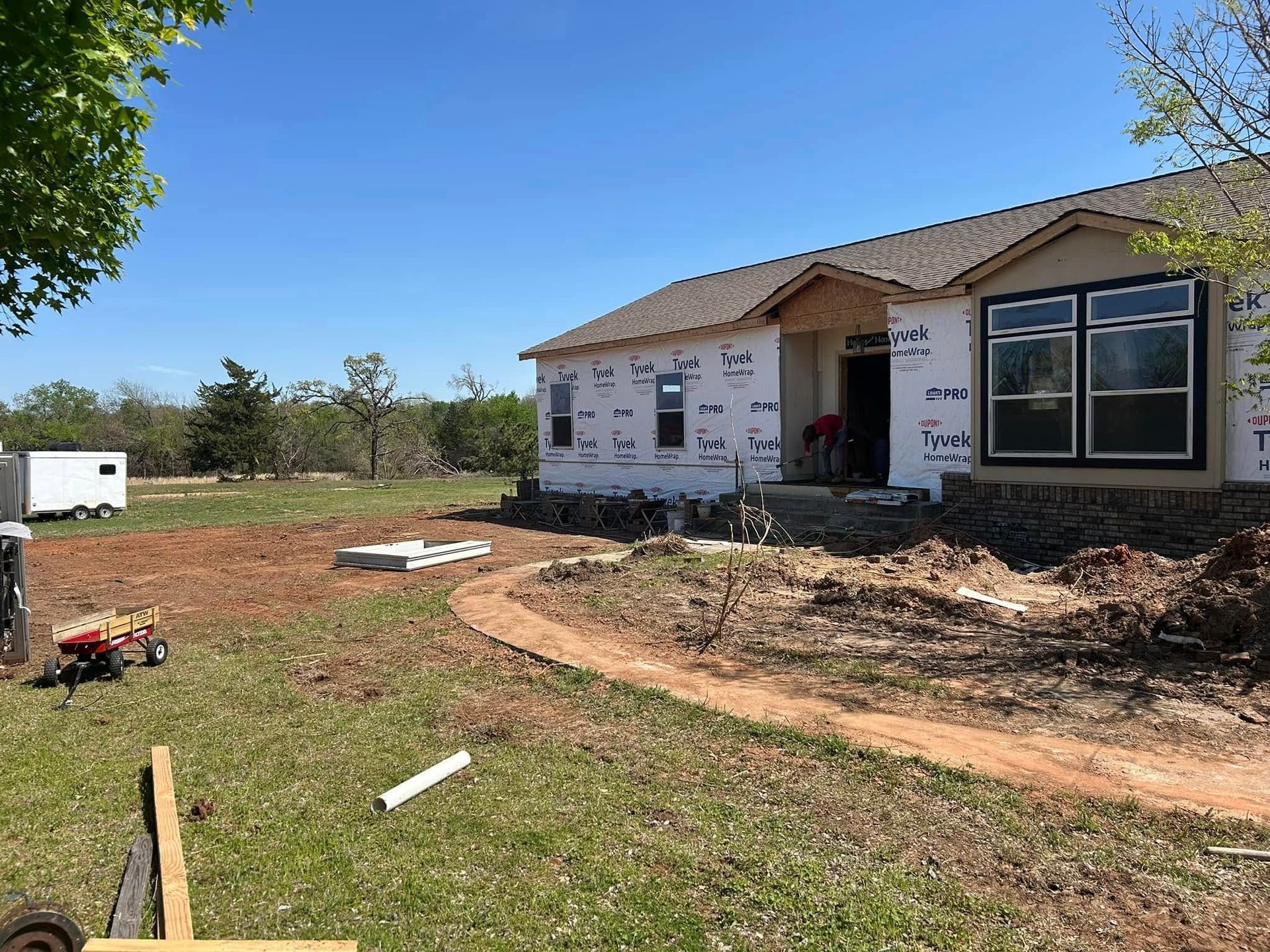 House under construction on a sunny day. Exterior wrapped, dirt path in yard, blue sky.