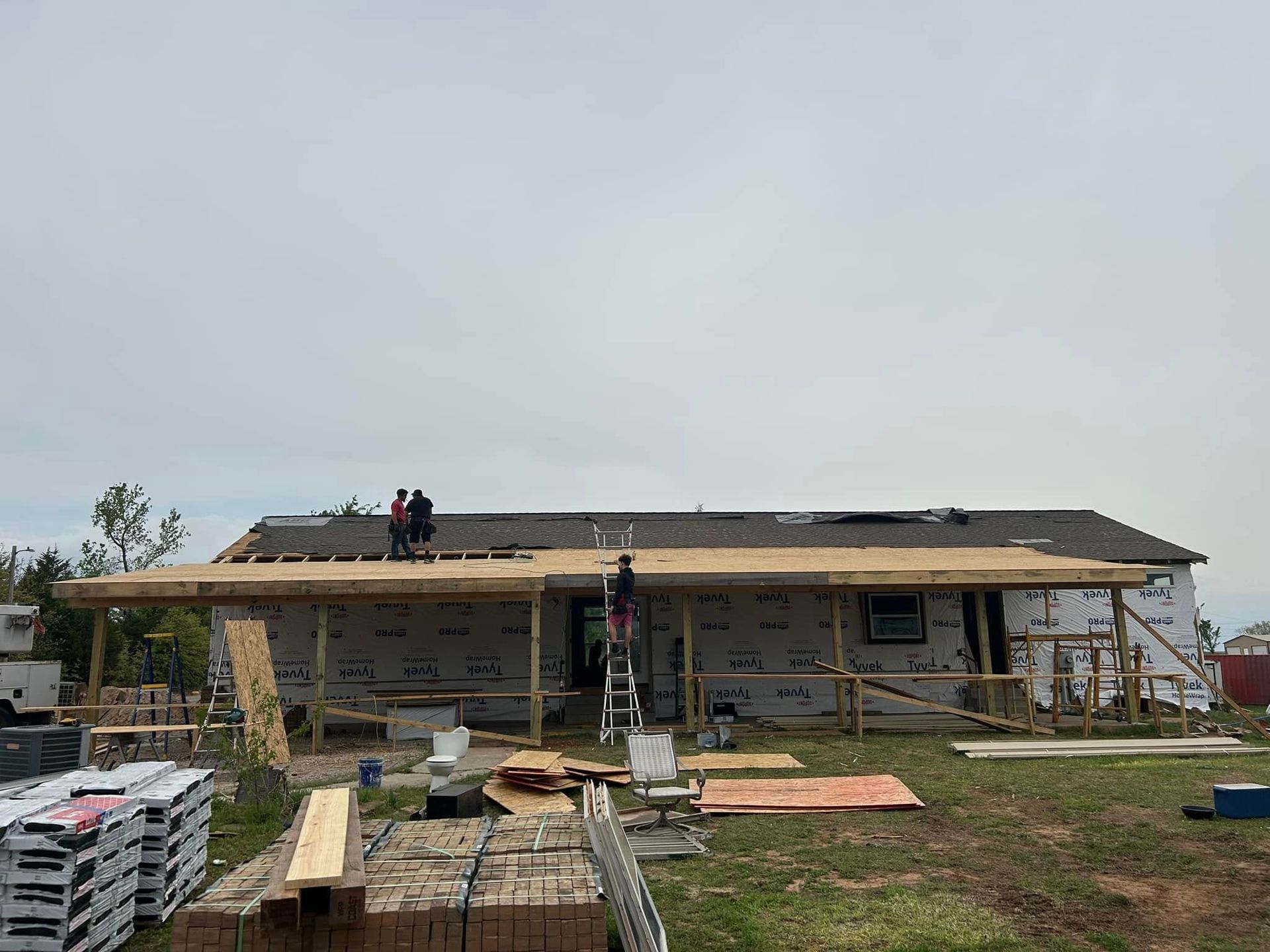 Construction workers on a new home roof, framing completed, under a cloudy sky.