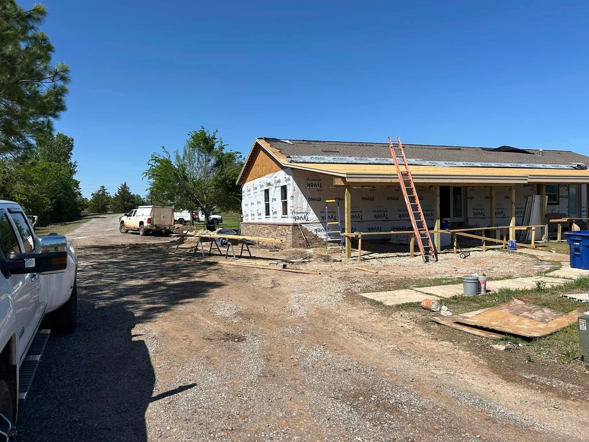 Construction of a house on a sunny day; exposed framing, wrap, and a ladder, with a truck in the foreground.