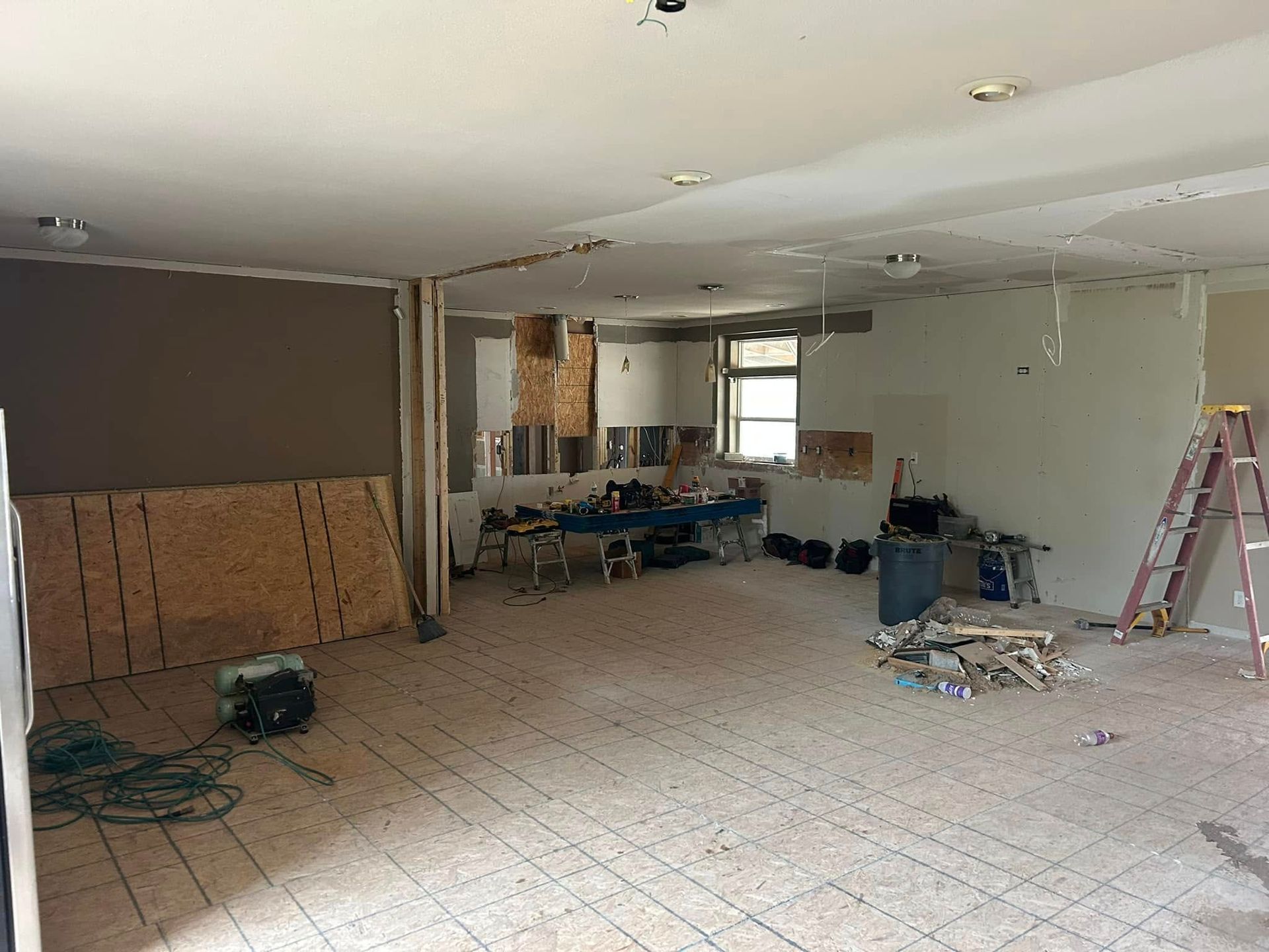 Room under renovation, unfinished walls, exposed studs and flooring. Construction tools, materials, and ladder present.
