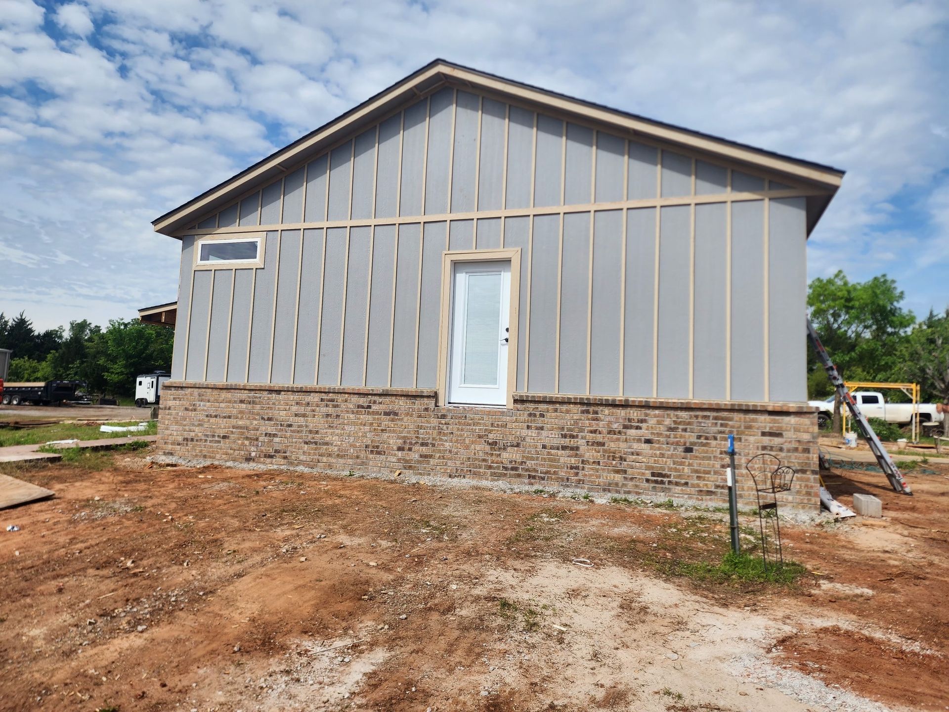 Building exterior under construction with gray siding, stone base, and door.