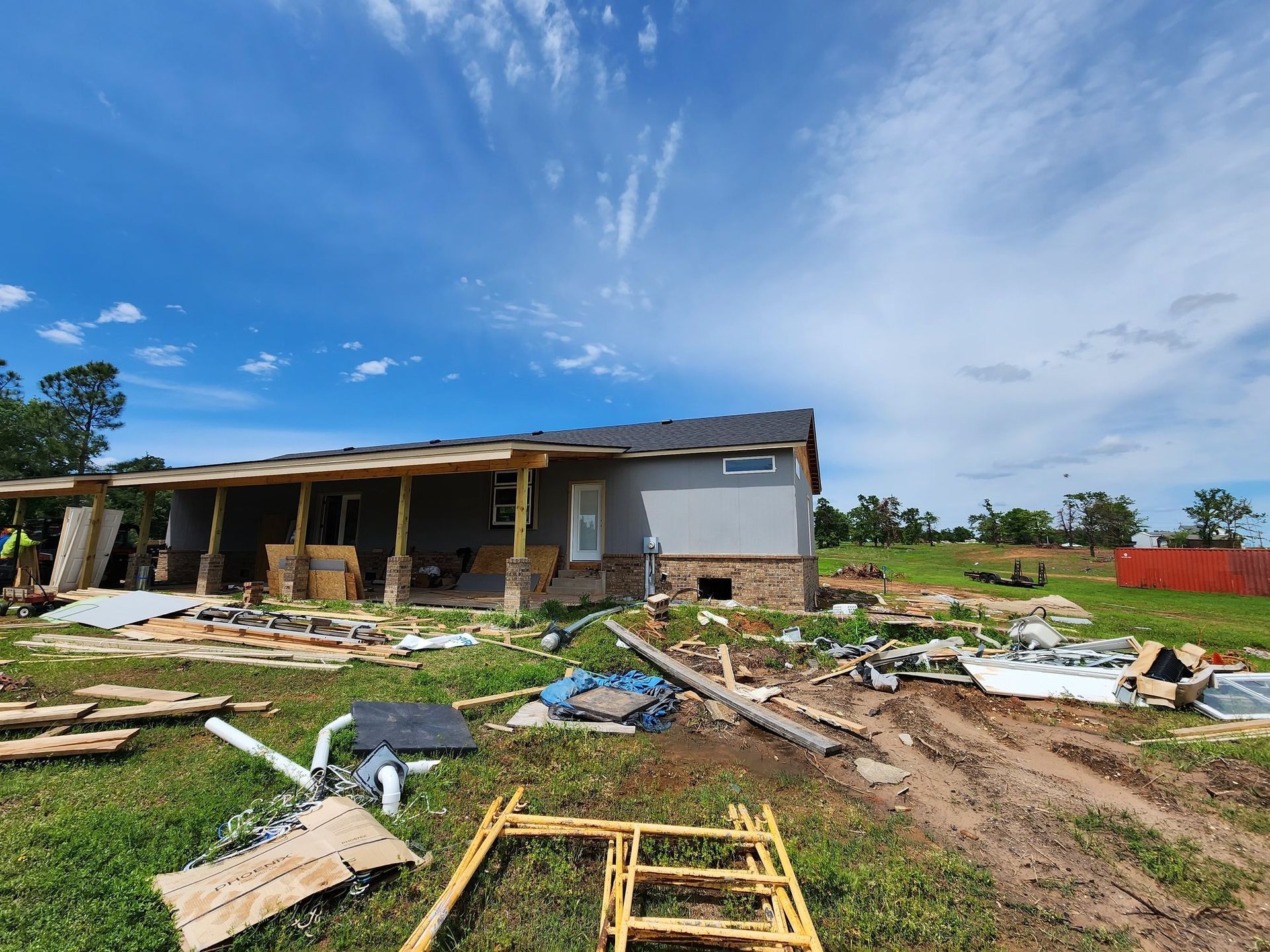 A house under construction with debris scattered on the lawn, under a blue sky with clouds.