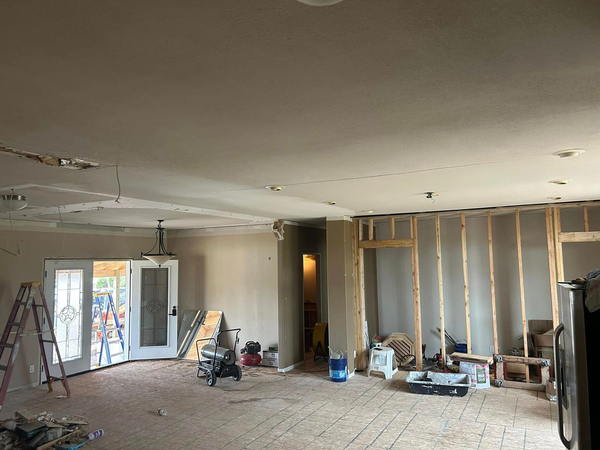 Interior renovation: walls framed, ceiling torn, debris on the floor, leading to doorways.