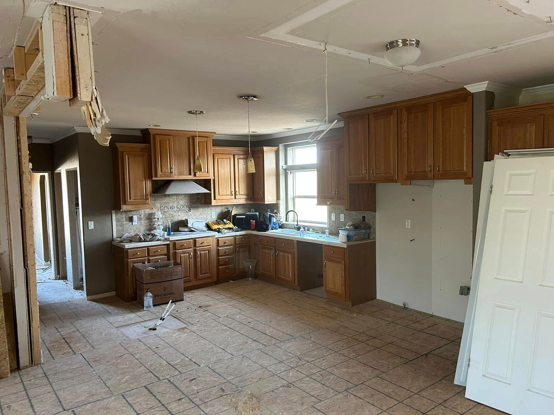 Kitchen under renovation with oak cabinets, exposed framing, and missing flooring.