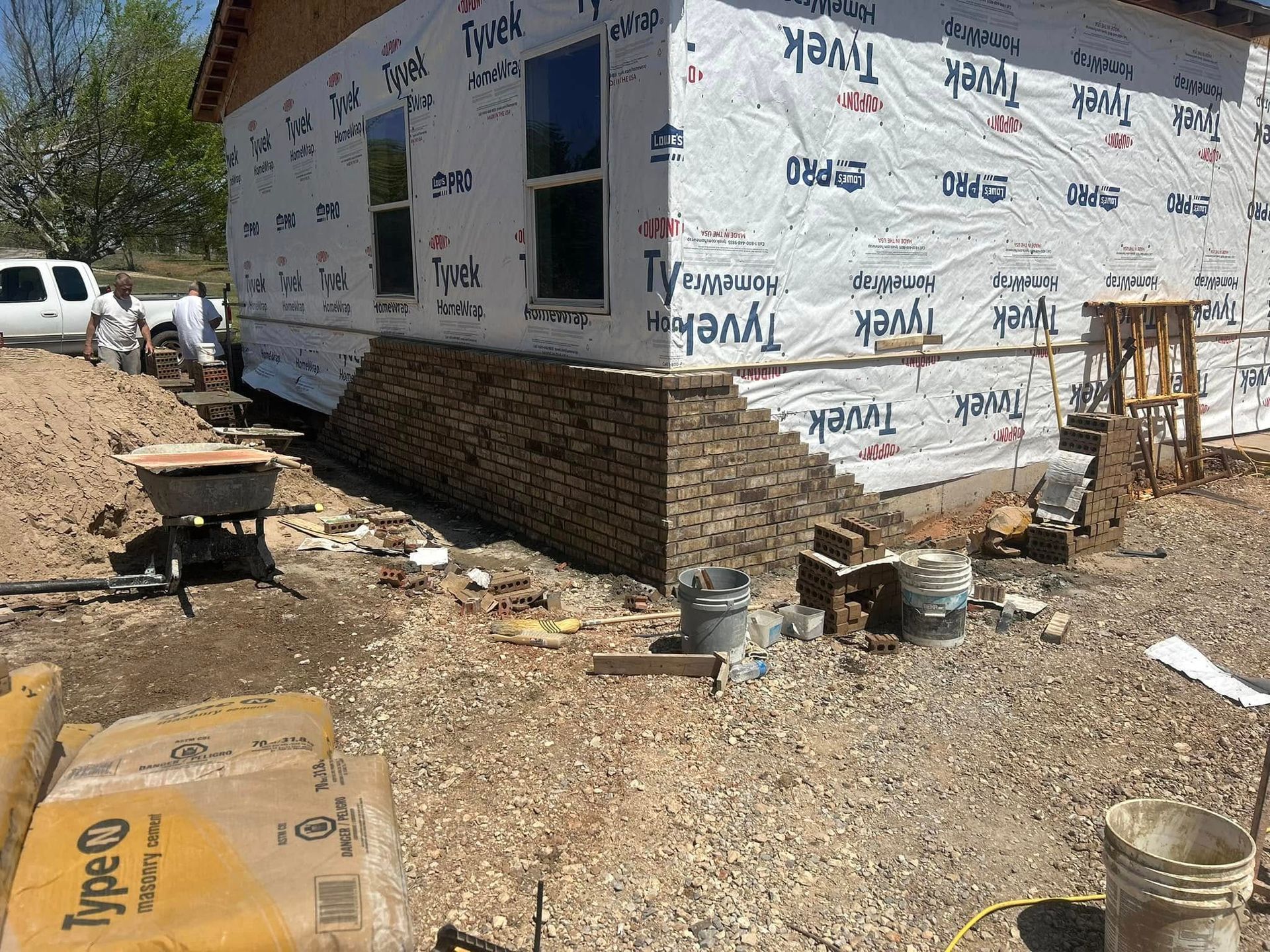 Brick masonry work on the corner of a house under construction, surrounded by gravel and supplies.