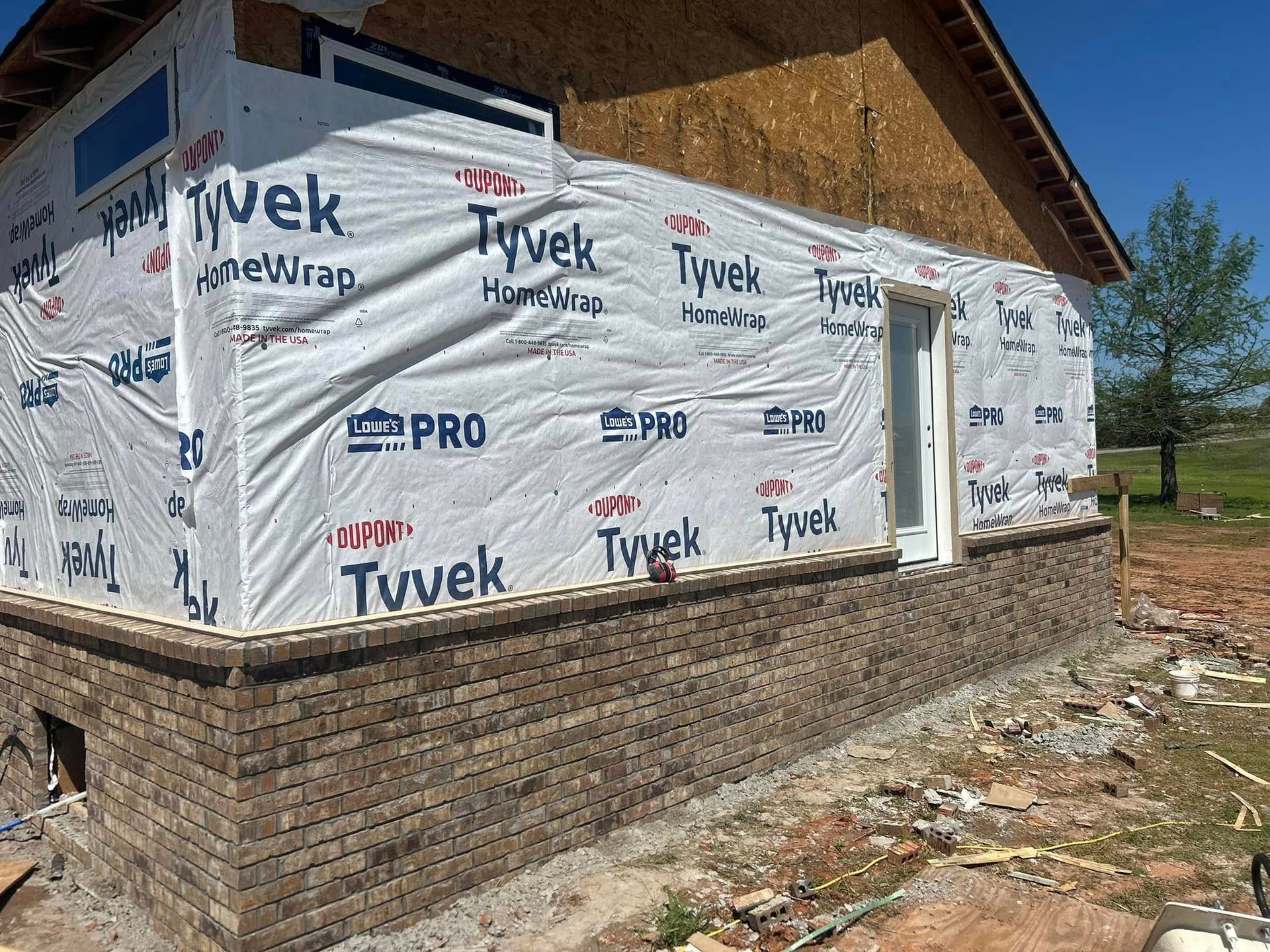 House under construction, brick base with Tyvek wrap, door, and exposed wood.