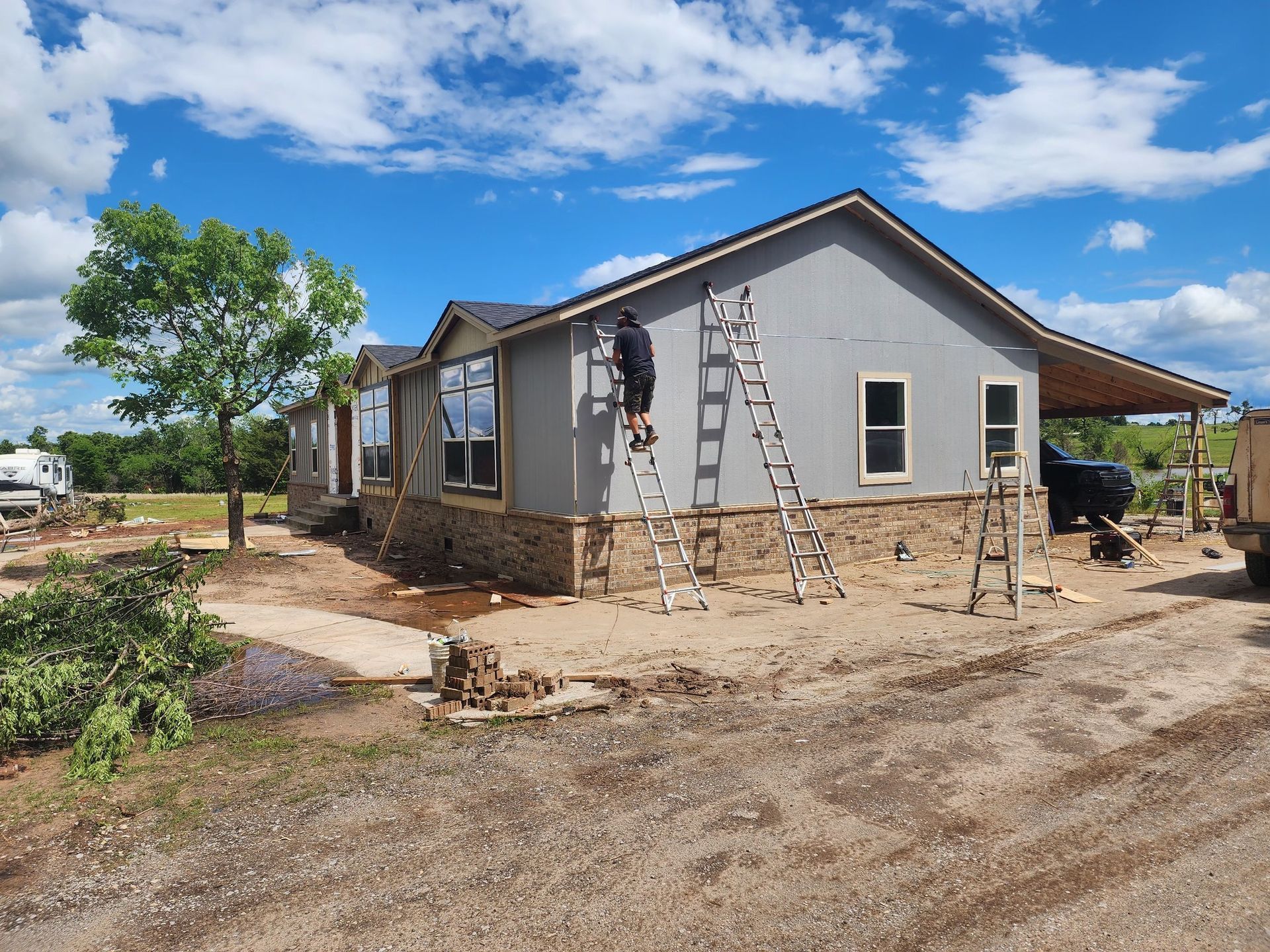 Workers siding a one-story house with stone and gray siding under a bright blue sky.
