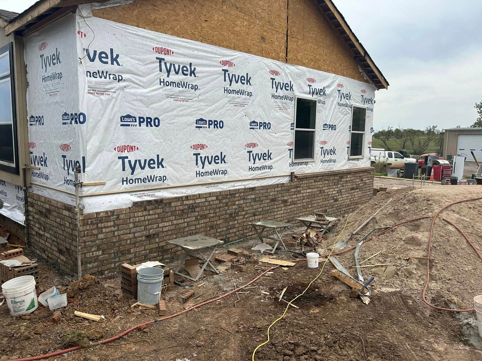 House under construction with brick facade, Tyvek wrap, windows, and dirt.