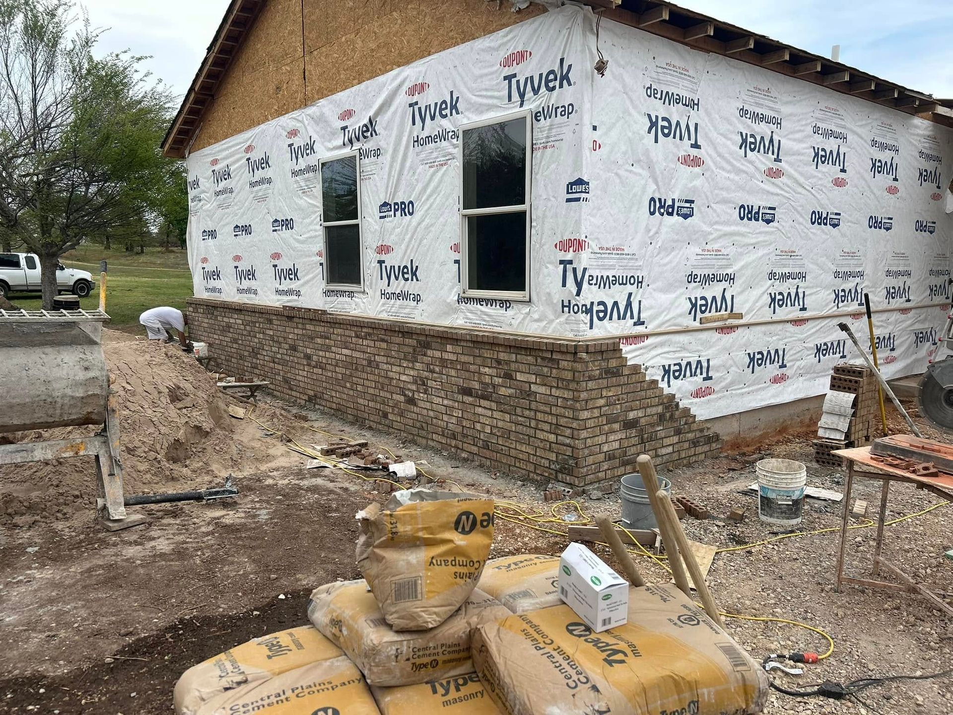 Construction site: House with stone veneer base, Tyvek wrap, two windows, and bags of cement.
