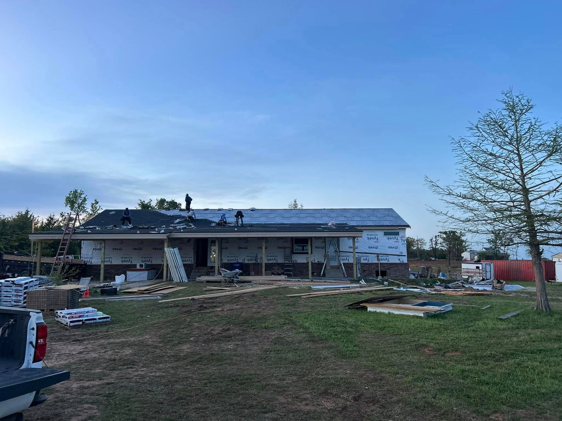Construction of a house with workers on the roof, surrounded by building materials, on a cloudy day.