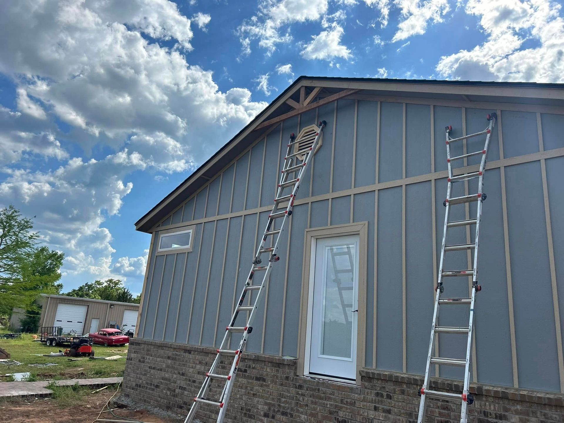 Construction site with two ladders leaning against a house with gray siding, under a cloudy sky.