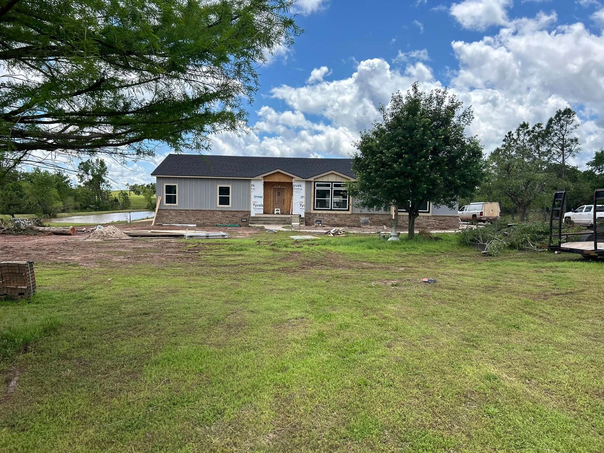 Construction of a gray home with brick facade in a grassy field, blue sky in the background.