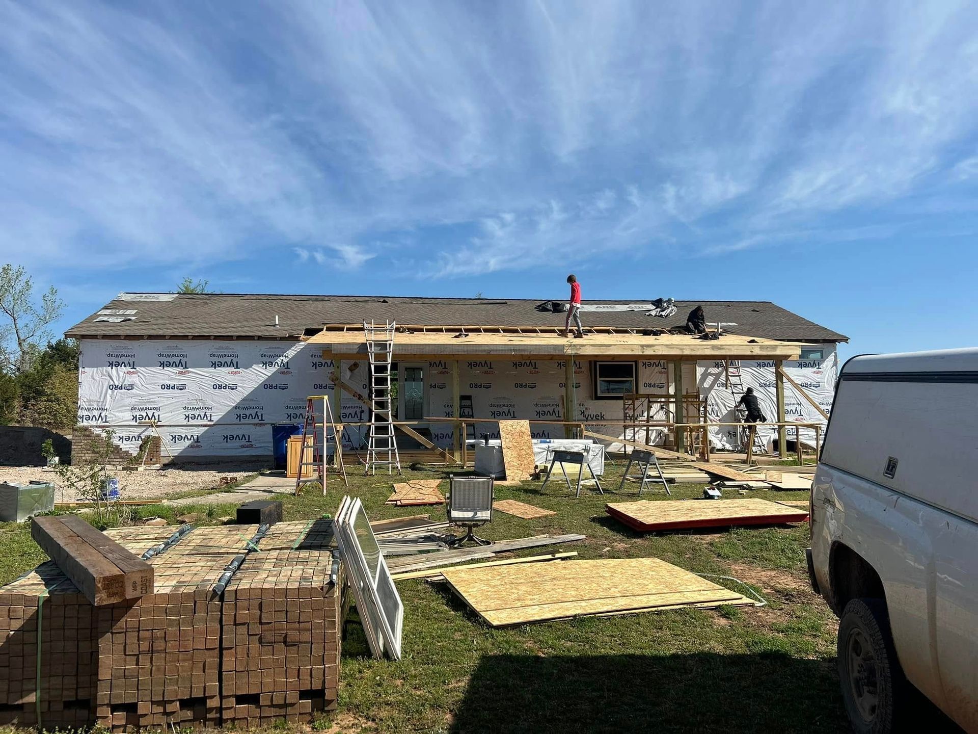 Construction site: Workers on a roof and building a porch extension on a house under a blue sky.