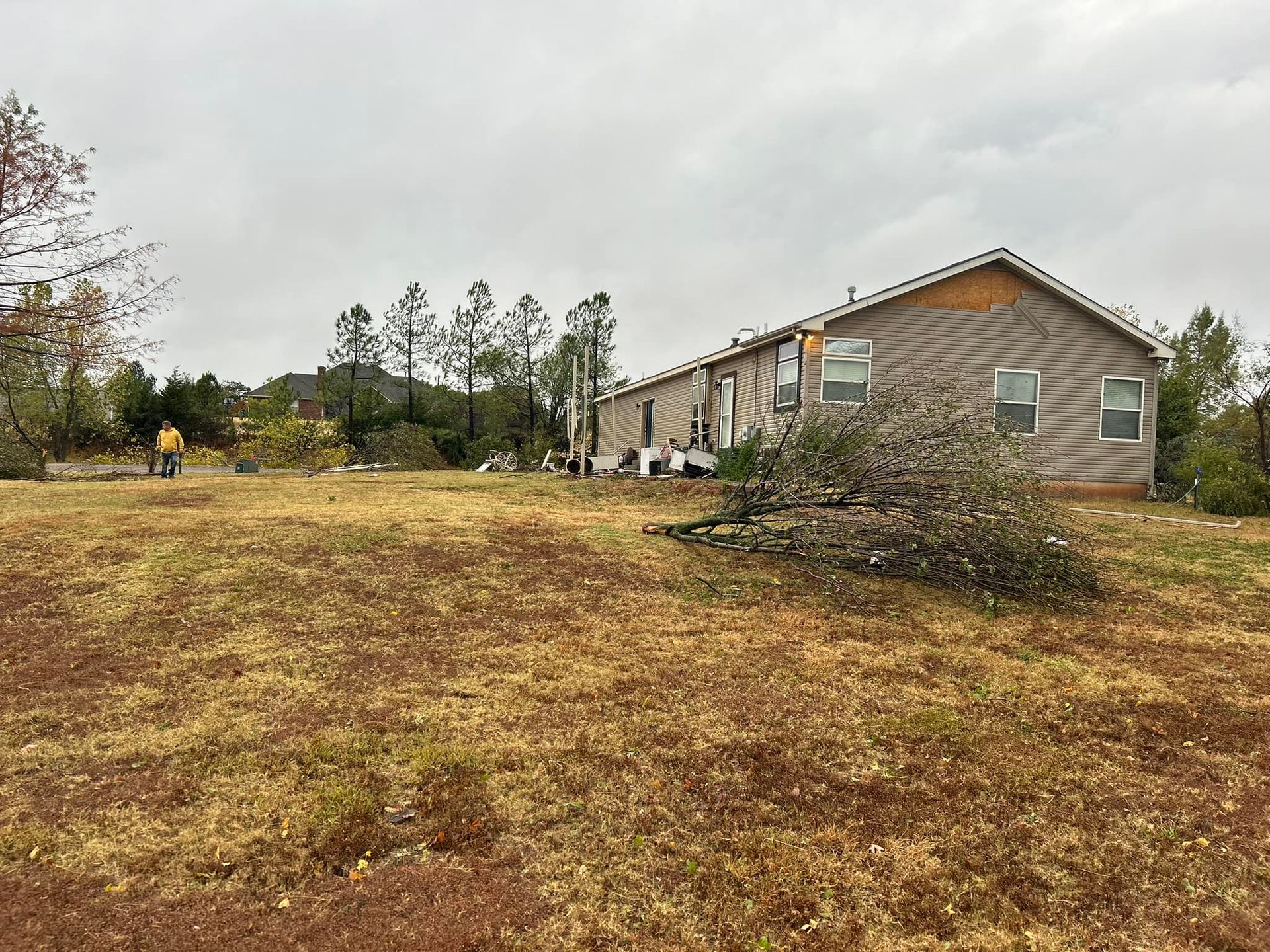 Mobile home damaged by wind; debris on the ground, cloudy sky.