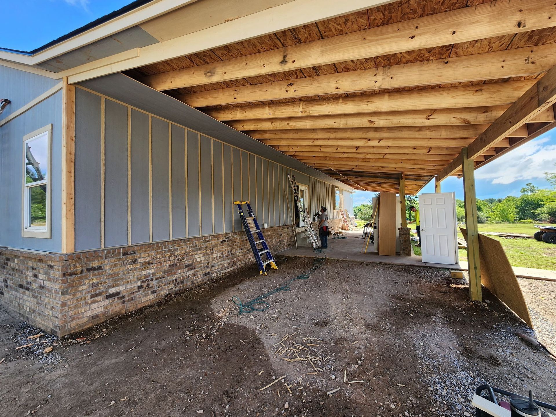 Construction of a home's exterior with blue siding, brick veneer, and a covered porch.