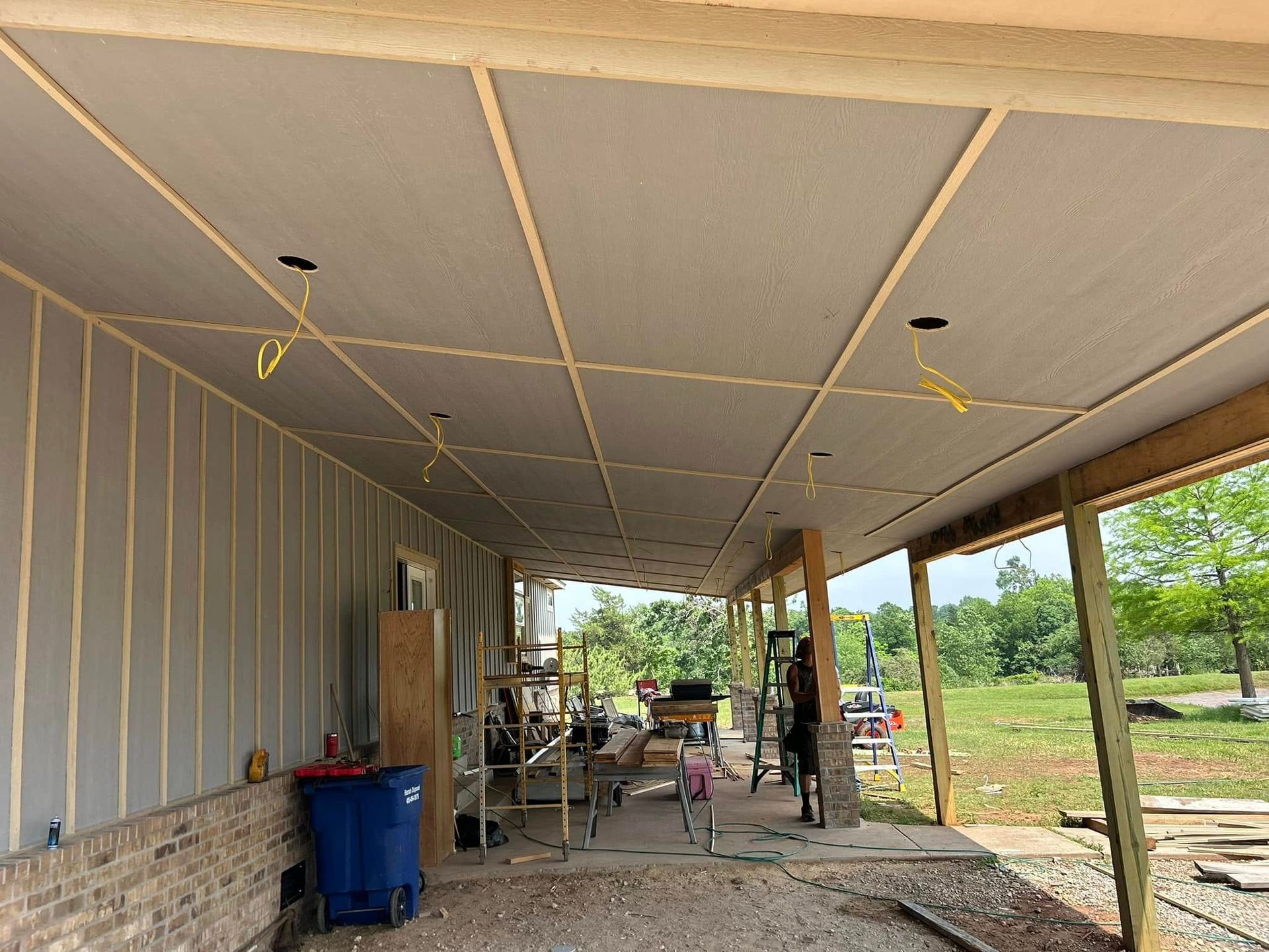 Construction of a covered porch with a completed ceiling. Yellow wires hang from light fixtures.