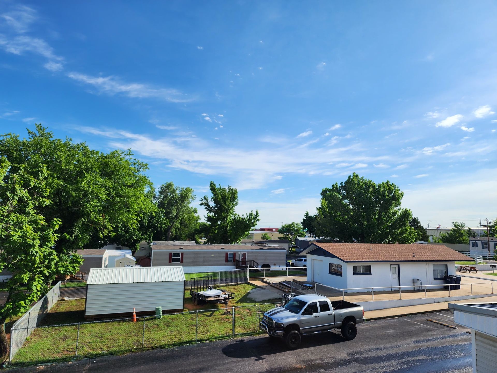 Mobile homes and trees under a bright blue sky with a truck parked in front.
