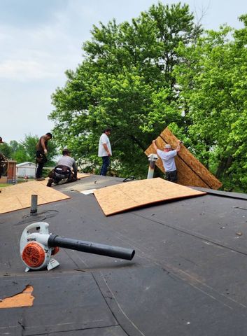 Roofers replacing plywood on a flat roof, using a leaf blower. Workers are visible.