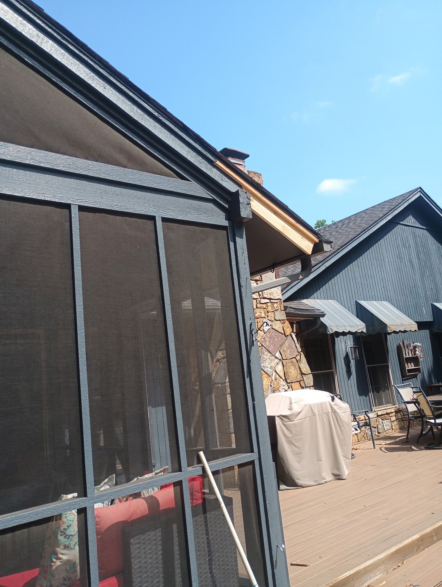 Screened porch with a house, deck, and blue sky in the background.