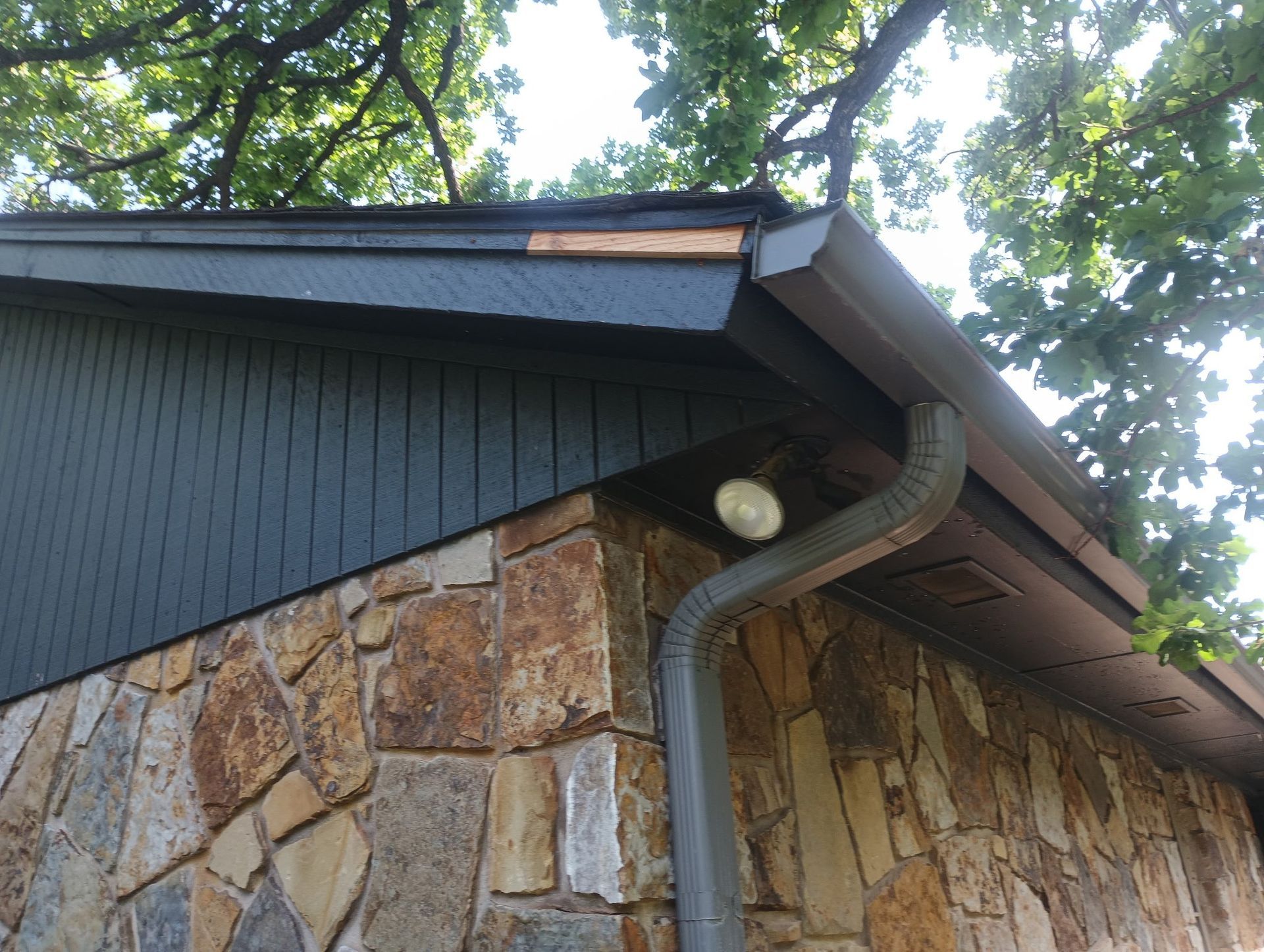 Stone house exterior with dark blue siding and trim, damaged roof edge, and a gray gutter.