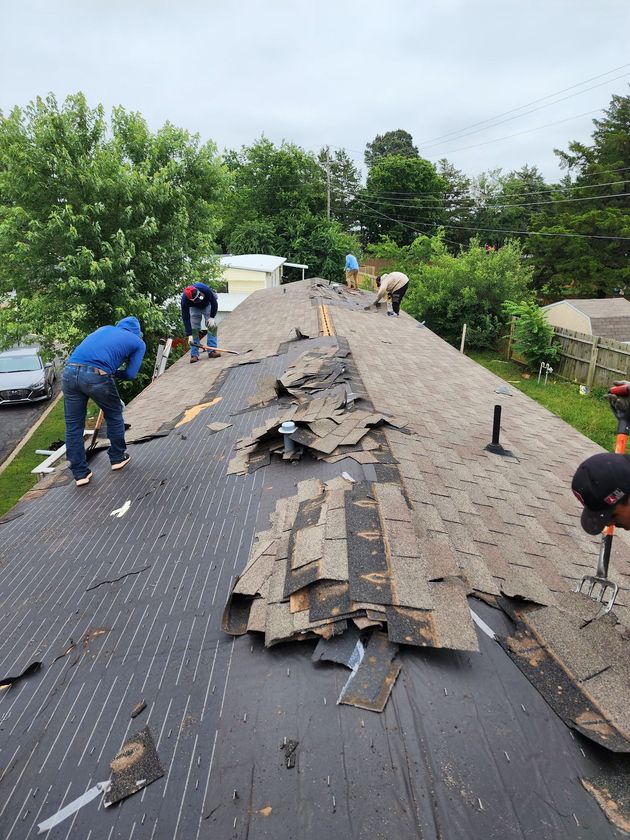 Roofers removing old shingles from a house roof on an overcast day.