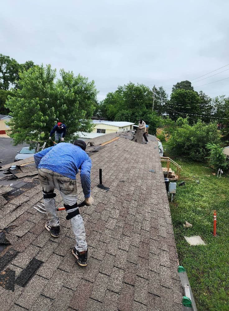 Construction workers installing shingles on a roof under cloudy skies.