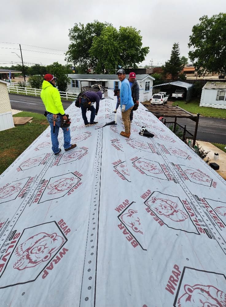 Roofers install roofing material on a mobile home under an overcast sky.