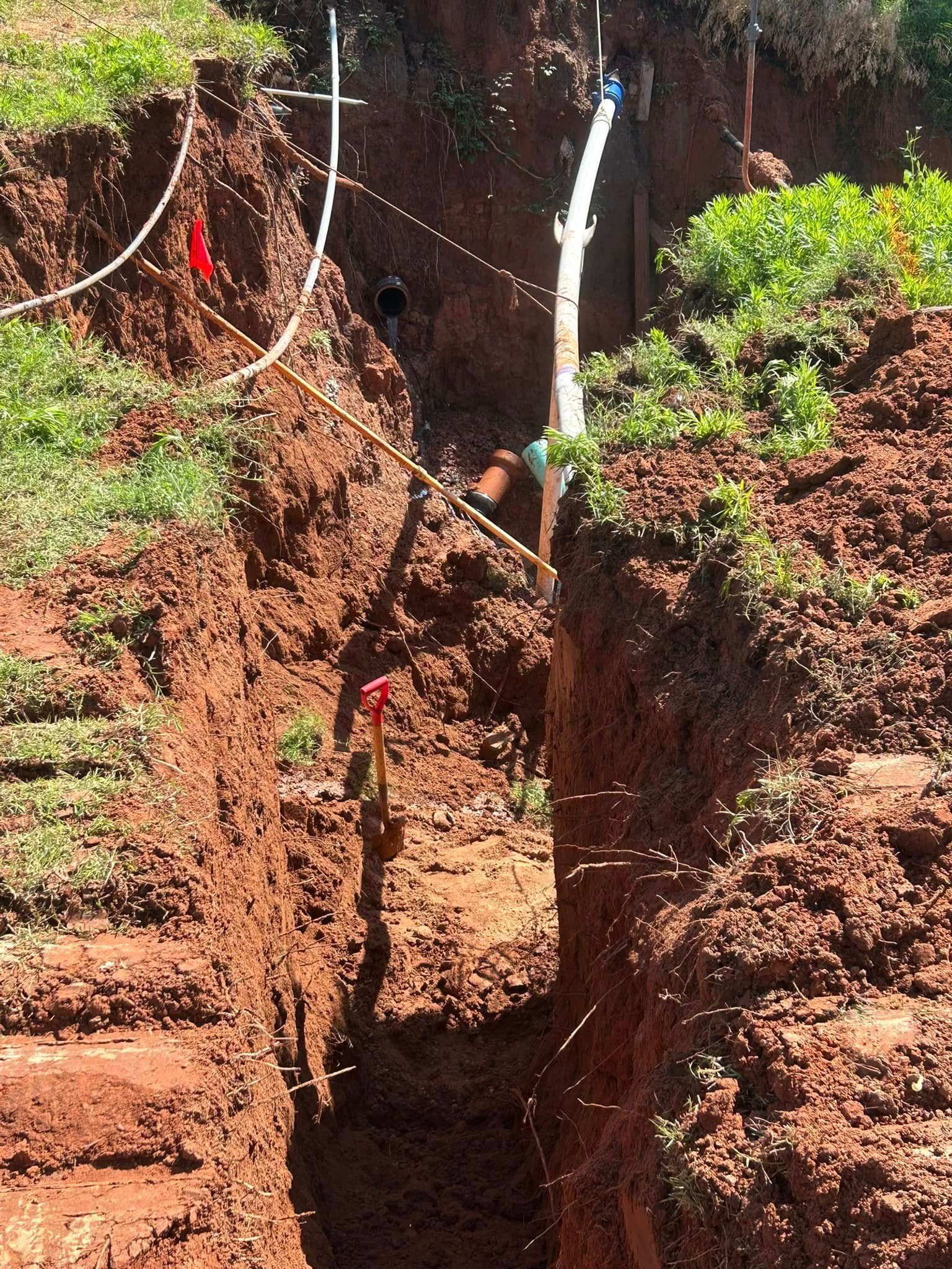 A deep trench cut into red earth, with pipes and lines installed.