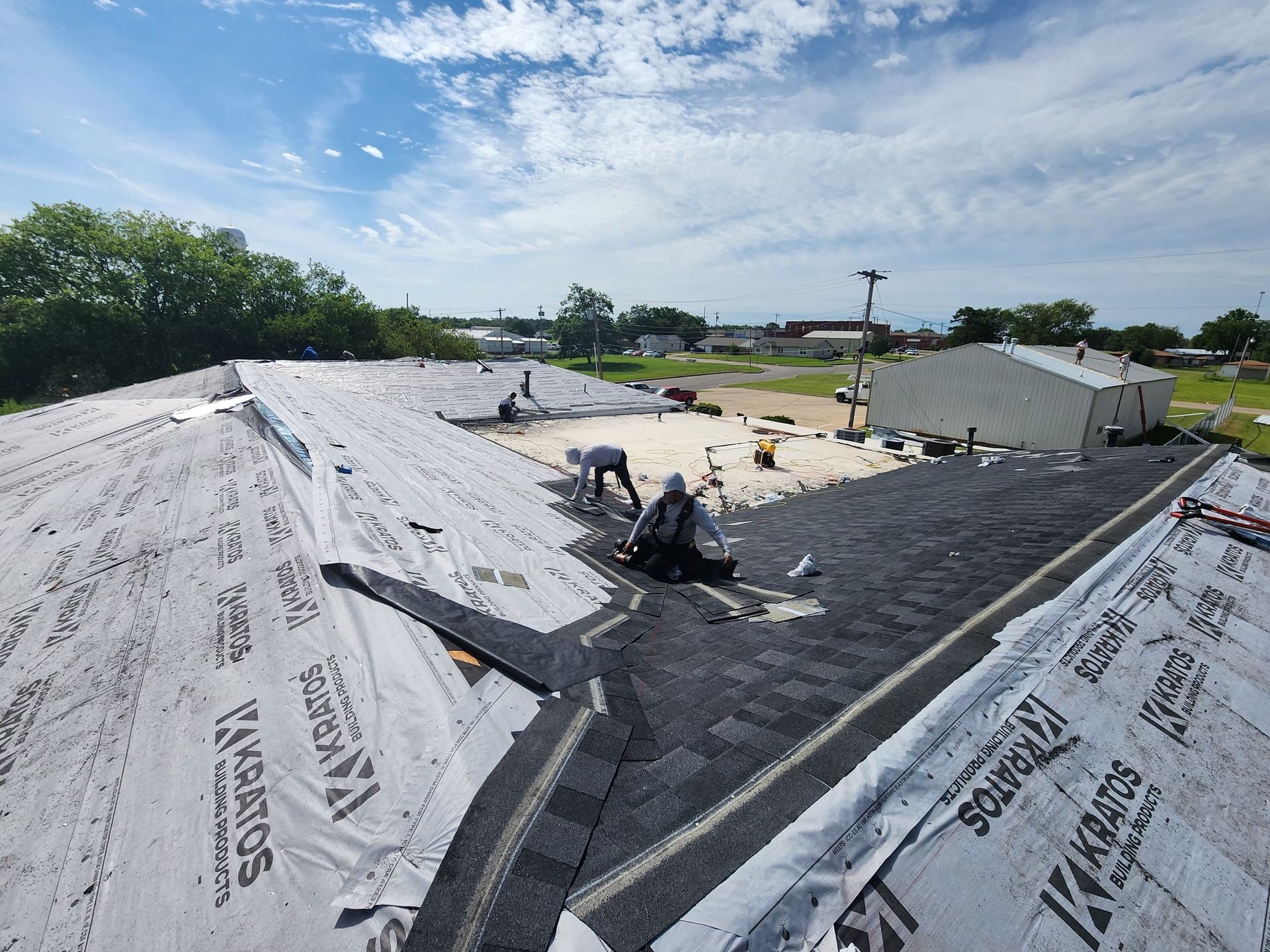 Roofers installing shingles on a building under a cloudy sky.