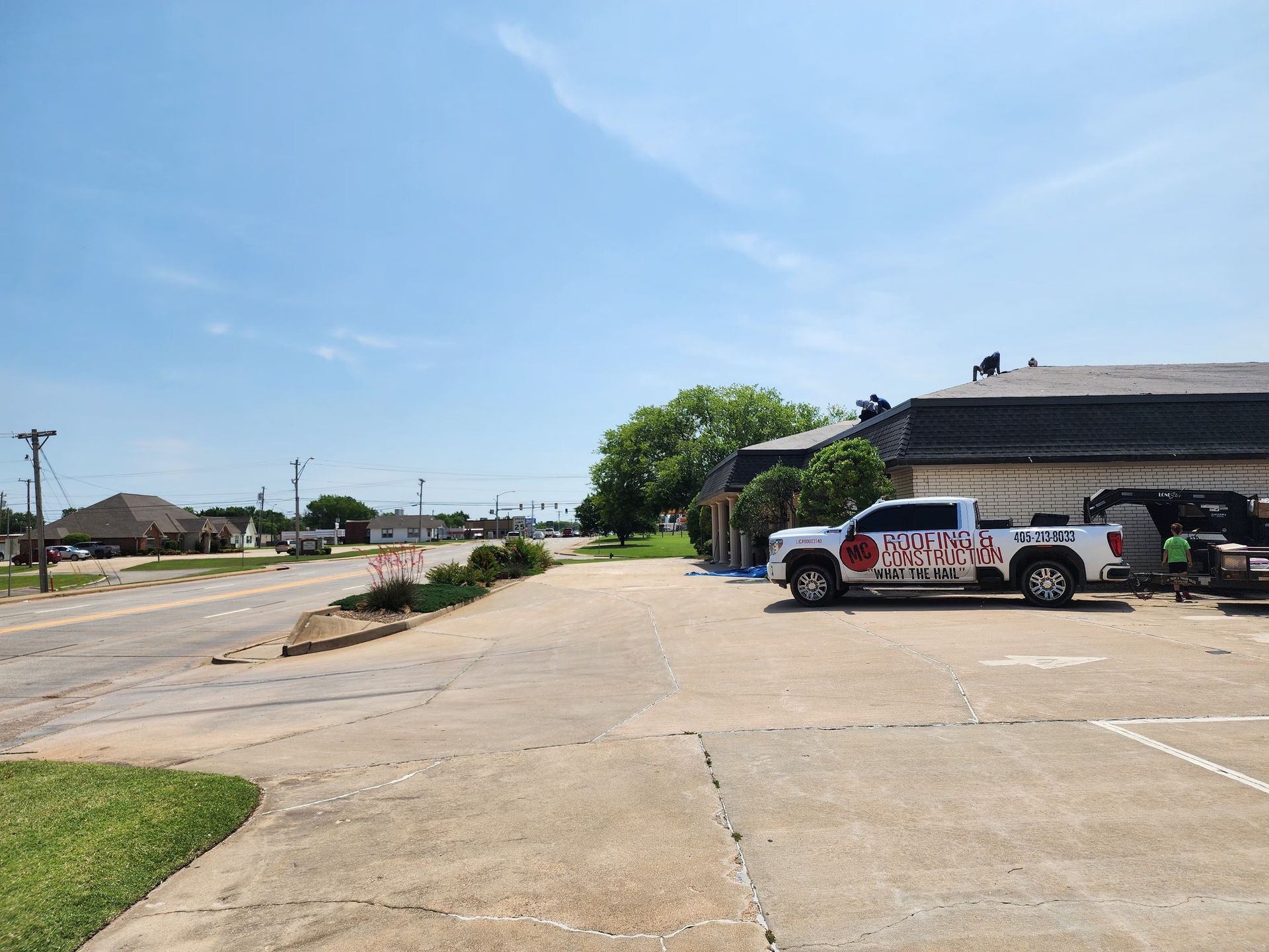 A white truck parked near a building with workers on the roof, on a sunny day.