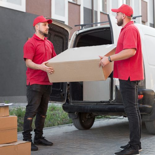 A man in a red shirt is holding a cardboard box in front of a van.
