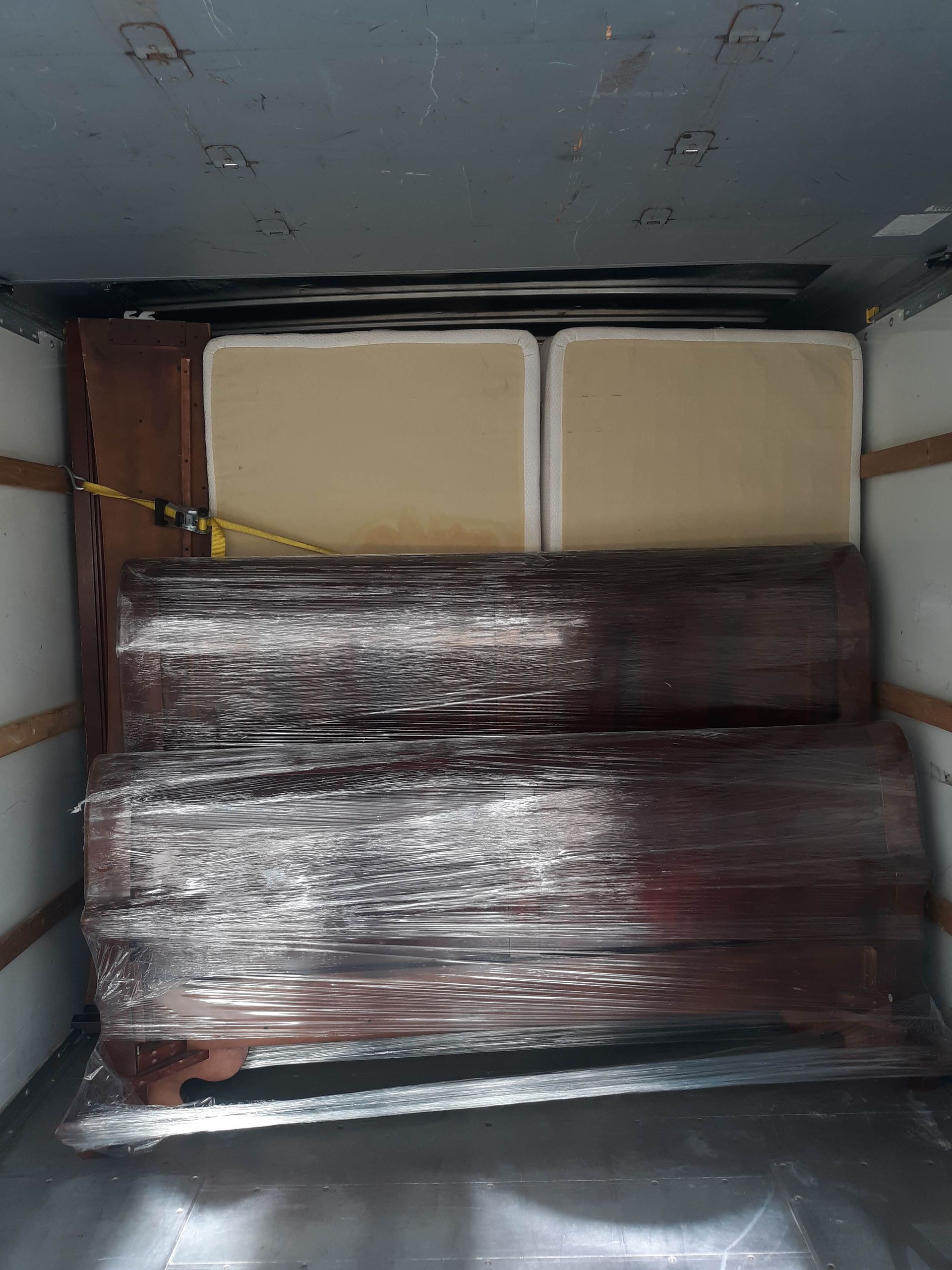 The inside of a moving truck filled with furniture wrapped in plastic.