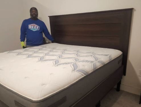 A man in a blue shirt is standing next to a bed.