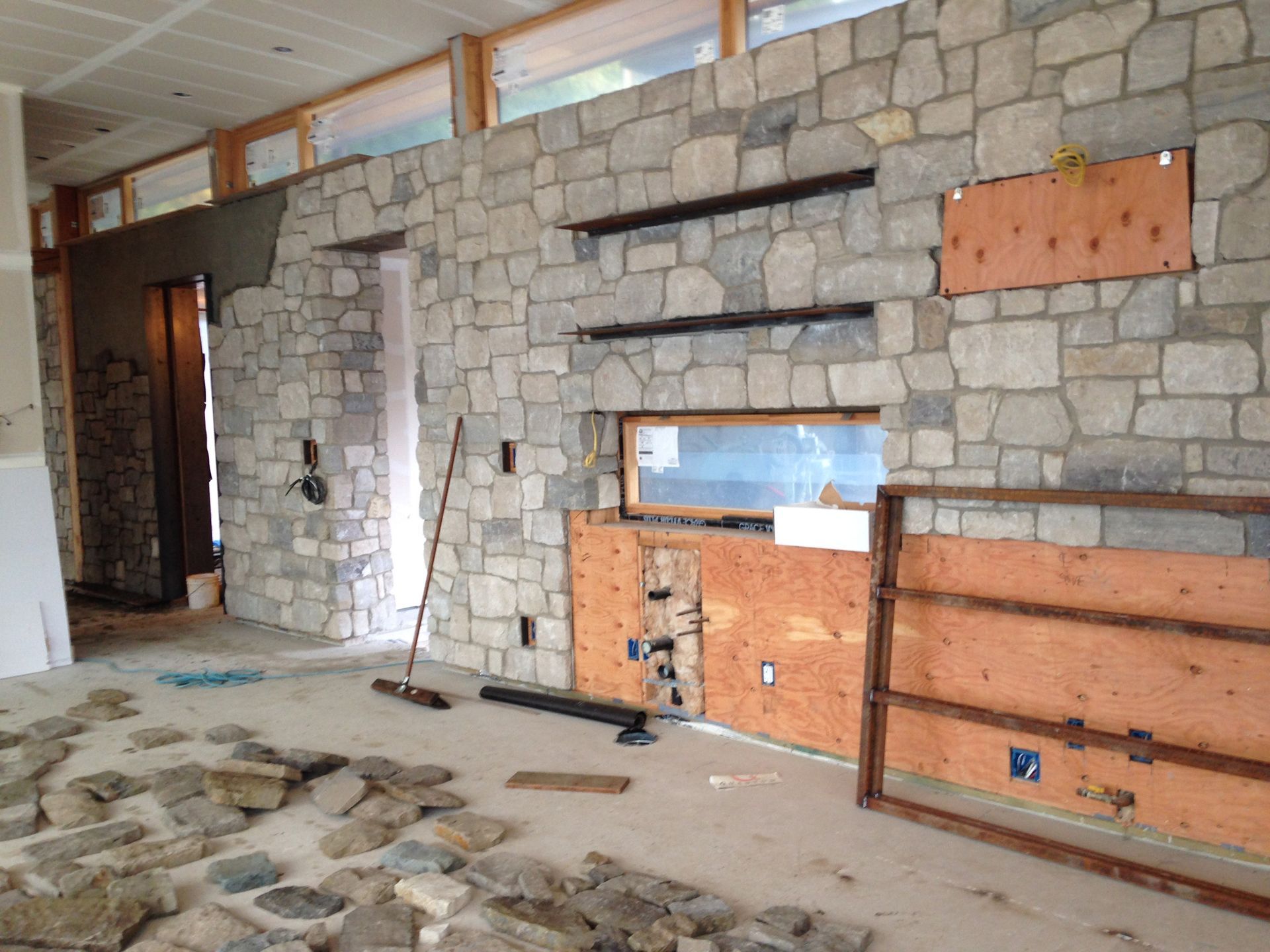 Interior wall under renovation with exposed stone, wood framing, and scattered debris on the floor