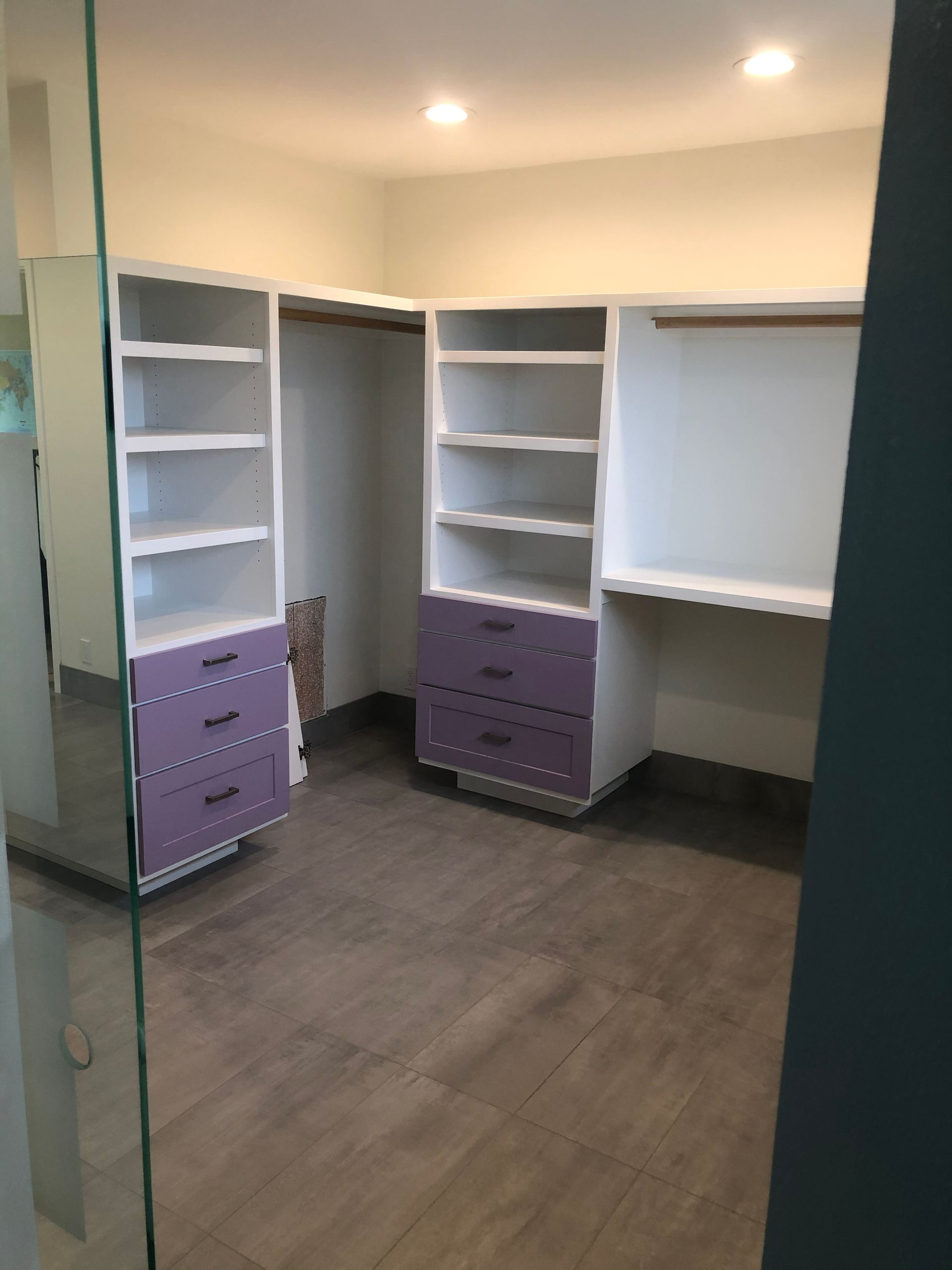 Empty walk-in closet with white shelves and purple drawers on dark wood flooring.